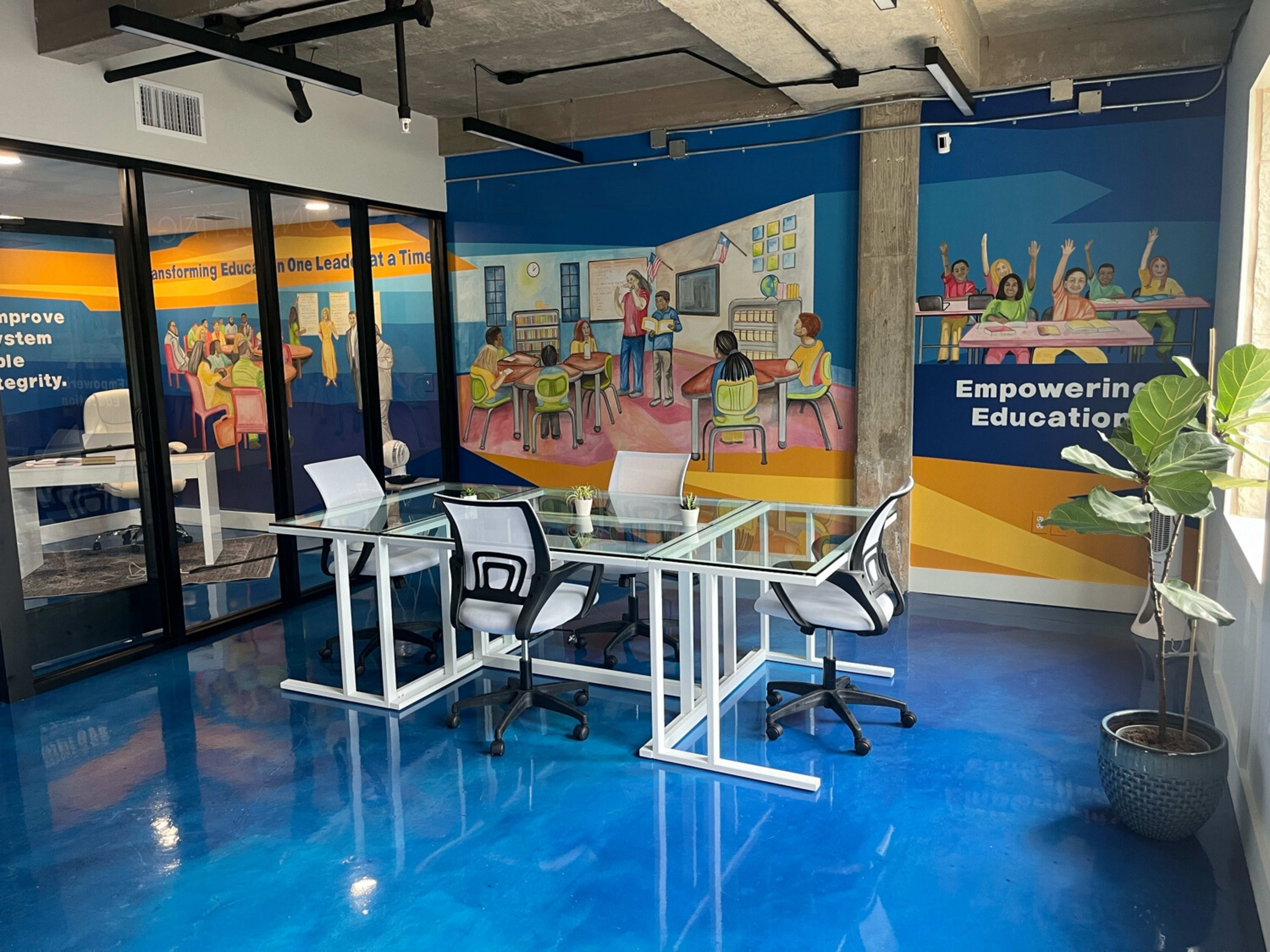 The image shows a well-lit meeting room with a glass table and white chairs, featuring colorful murals on the walls related to education.