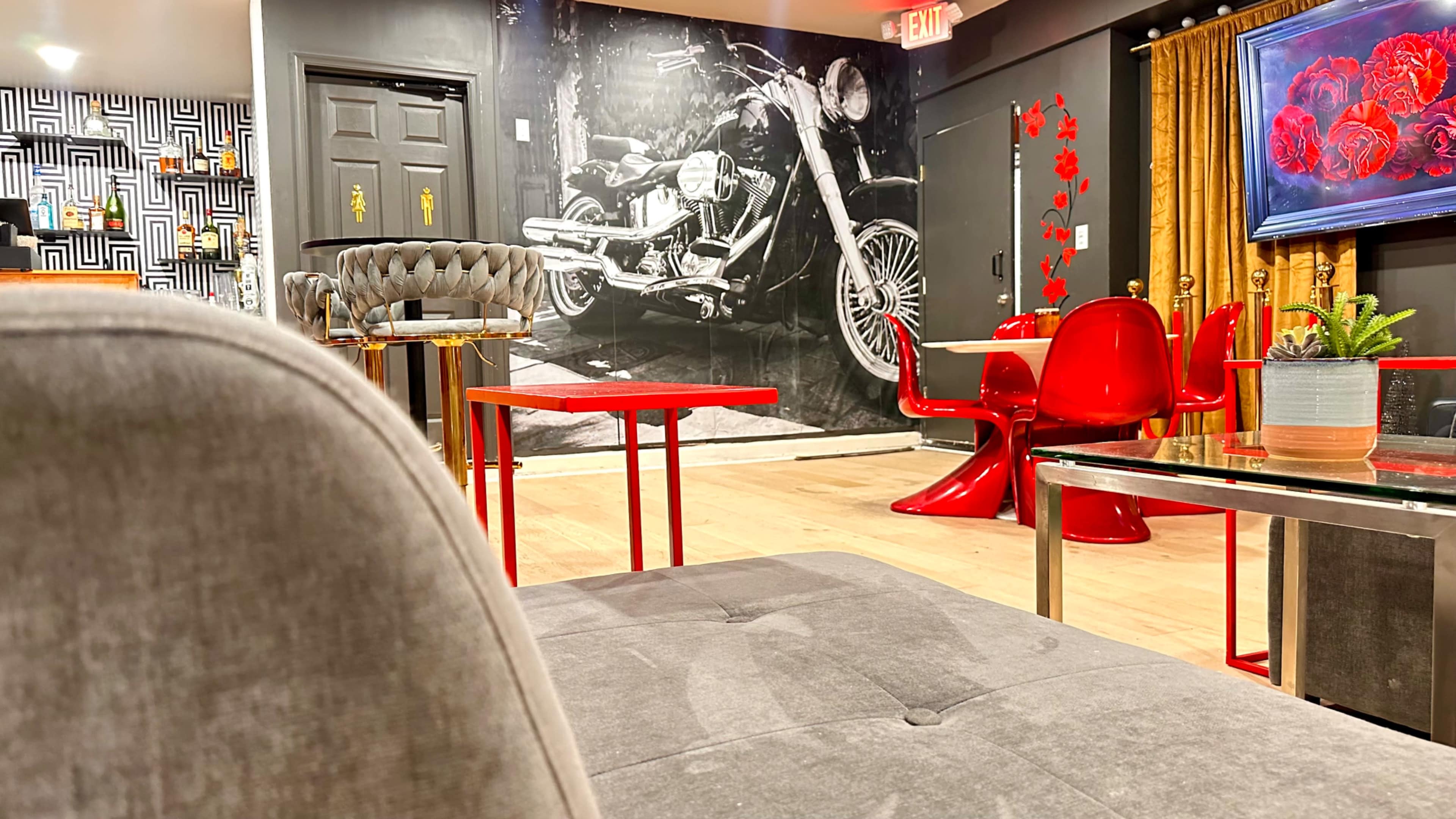 The image shows a stylish lounge area with modern red furniture, a large black-and-white motorcycle mural on the wall, and a cozy seating arrangement.