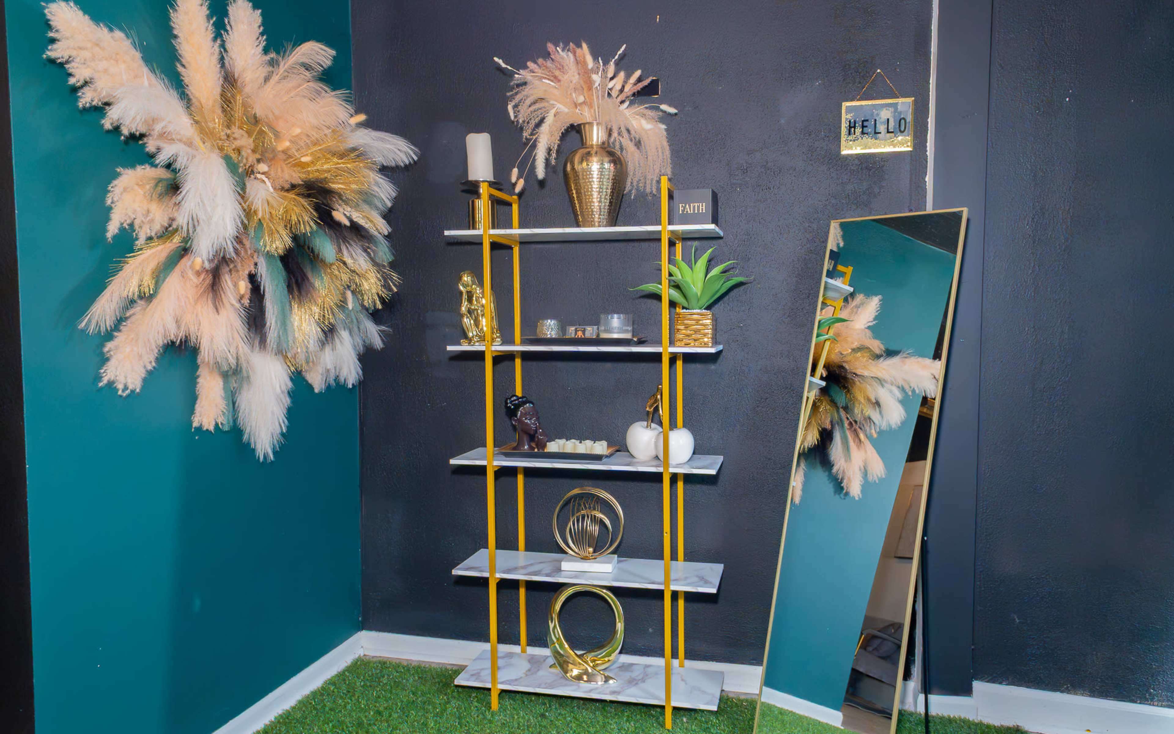 The image features a modern shelving unit with decorative items, including vases and sculptures, against a dark wall, complemented by a large mirror and wall decor made of dried plants.