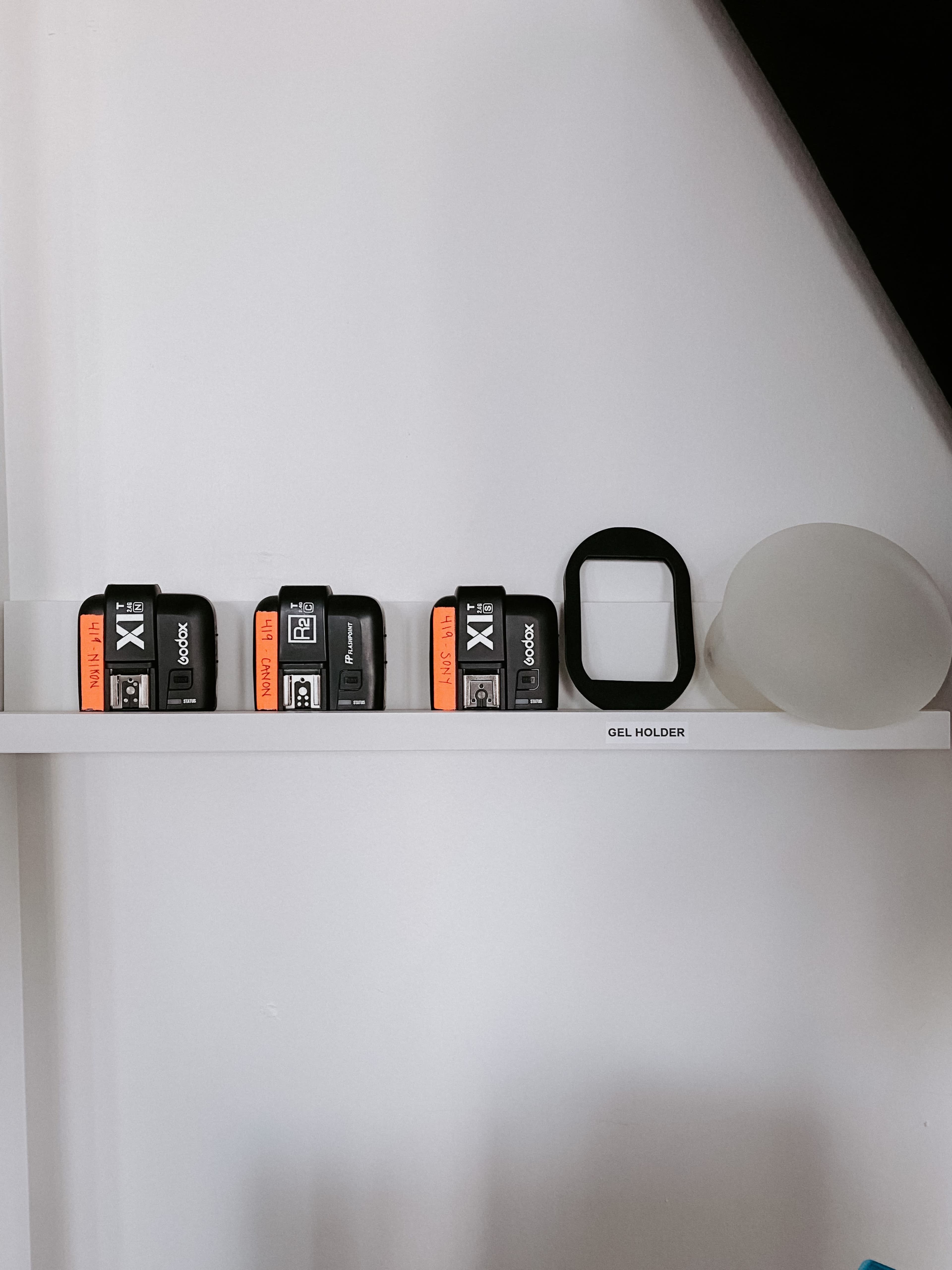 A shelf displays several black devices with orange labels, a white circular object, and a rectangular frame labeled "GEL HOLDER."