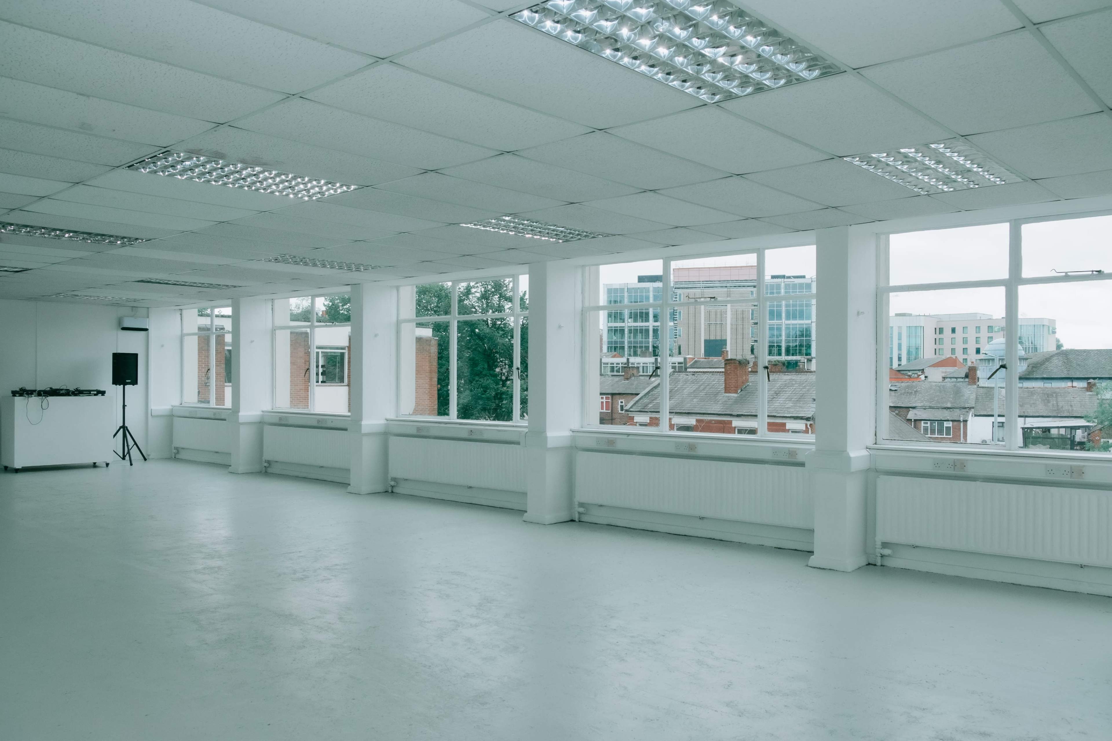 A spacious, vacant office interior with large windows providing natural light and a view of nearby buildings.