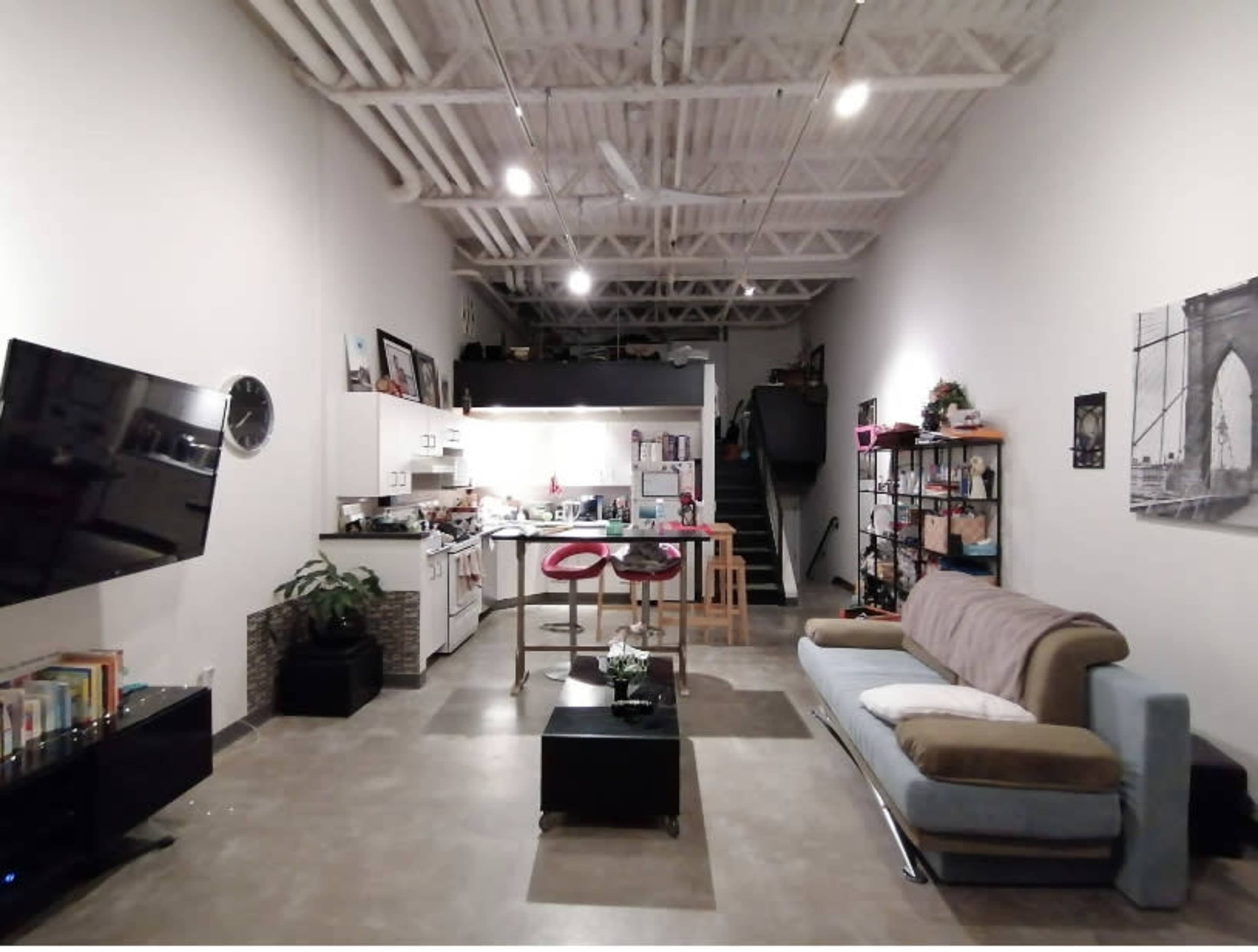 A spacious, modern open-concept living area with a kitchen, dining table, and a living room featuring a sofa and a television.