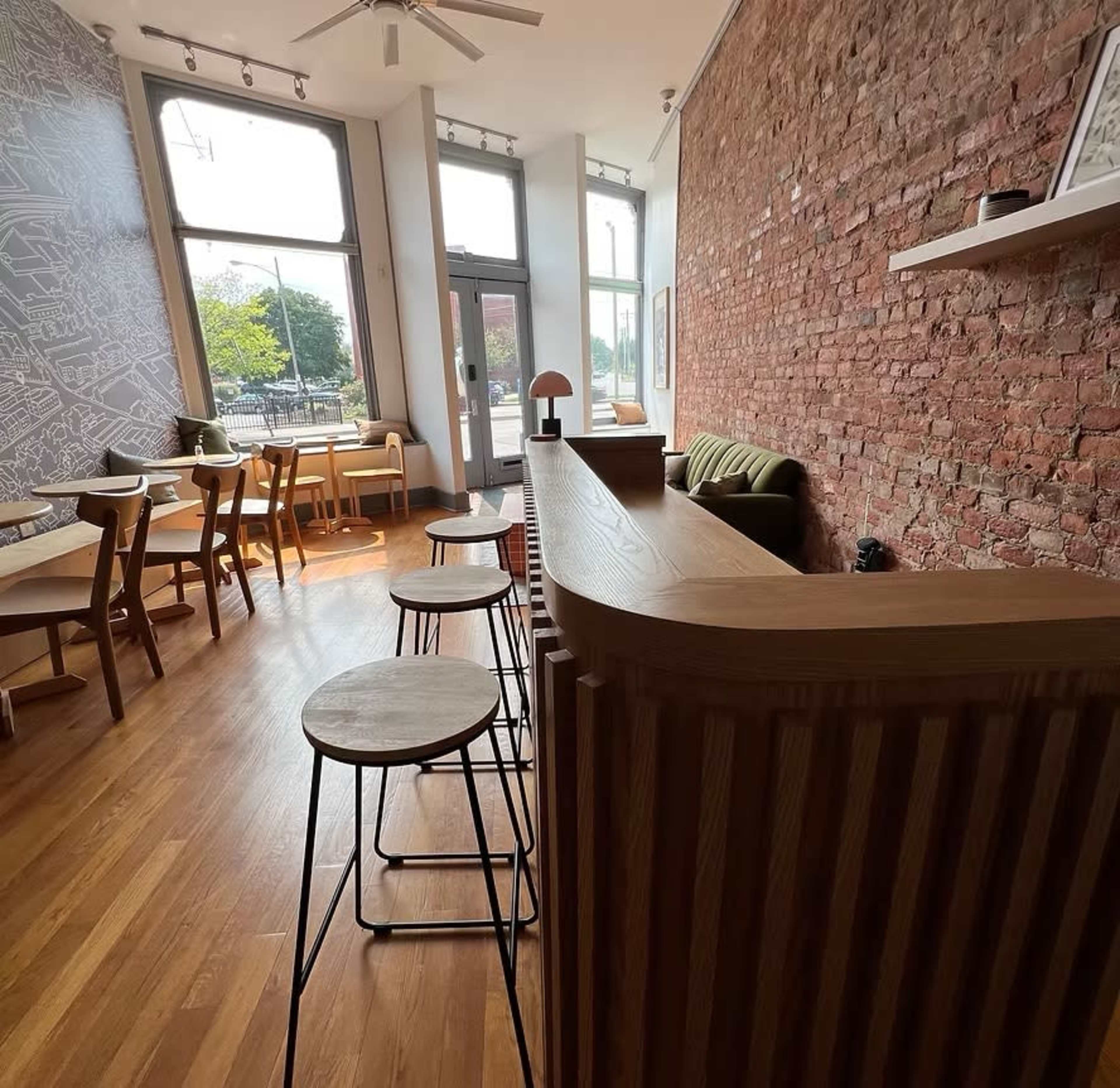 The image shows a modern café interior featuring exposed brick walls, wooden furniture, and a mixture of seating options, including bar stools at a counter.