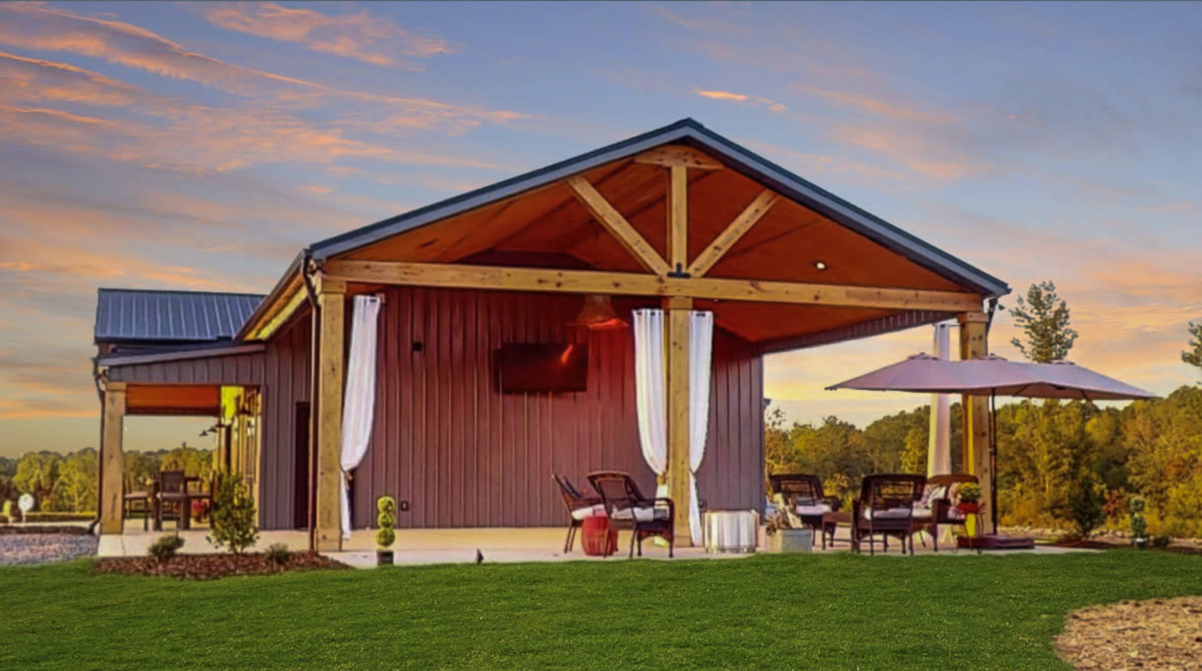 A modern barn-style building with a wide porch, surrounded by a grassy area and a few outdoor seating arrangements.
