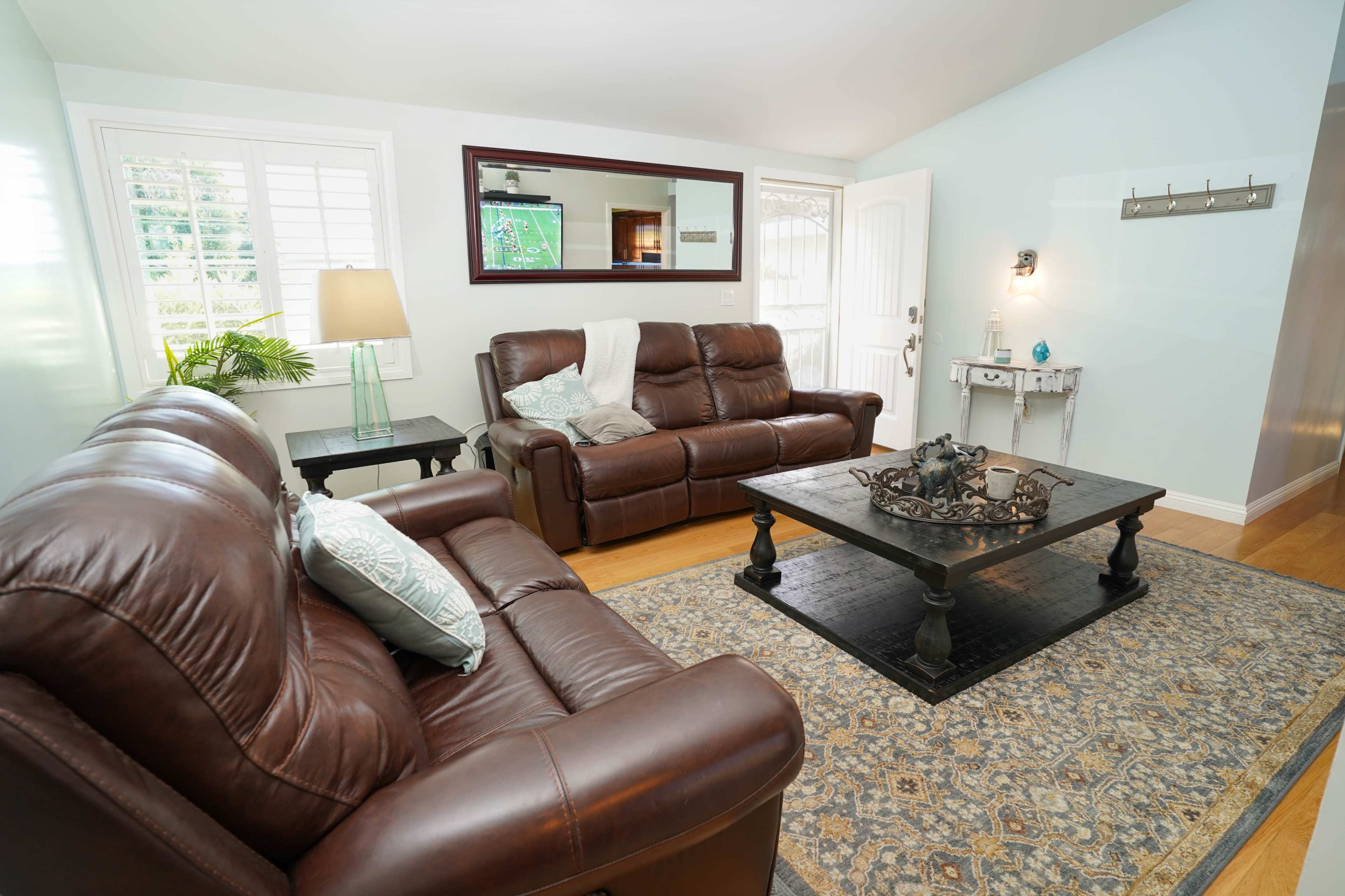 A living room with two brown leather sofas, a dark coffee table, and a rug, all illuminated by natural light coming through a window.