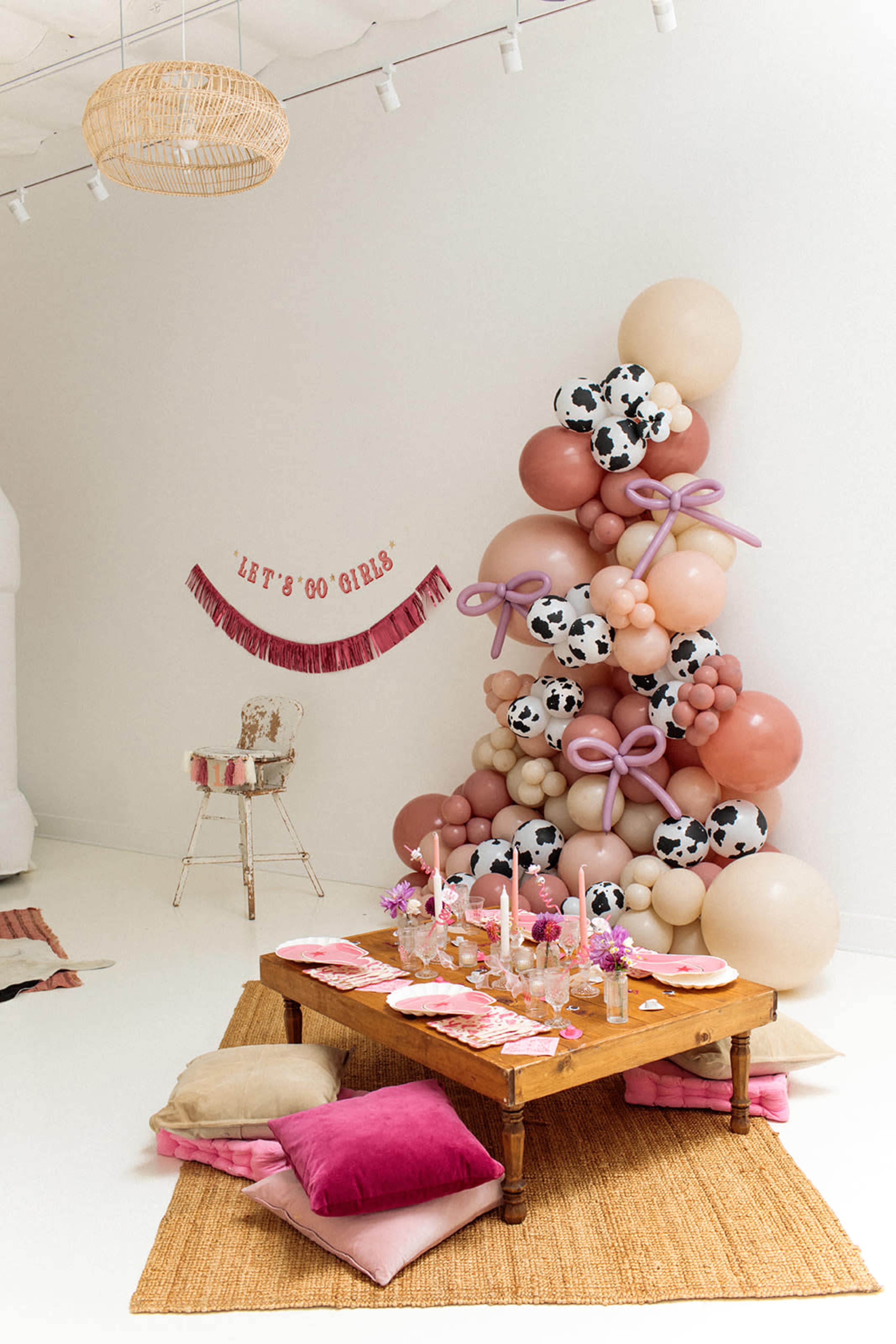 The scene features a festive setting with a decorated table and a balloon arrangement in the background, complete with cow print and pastel-colored balloons.