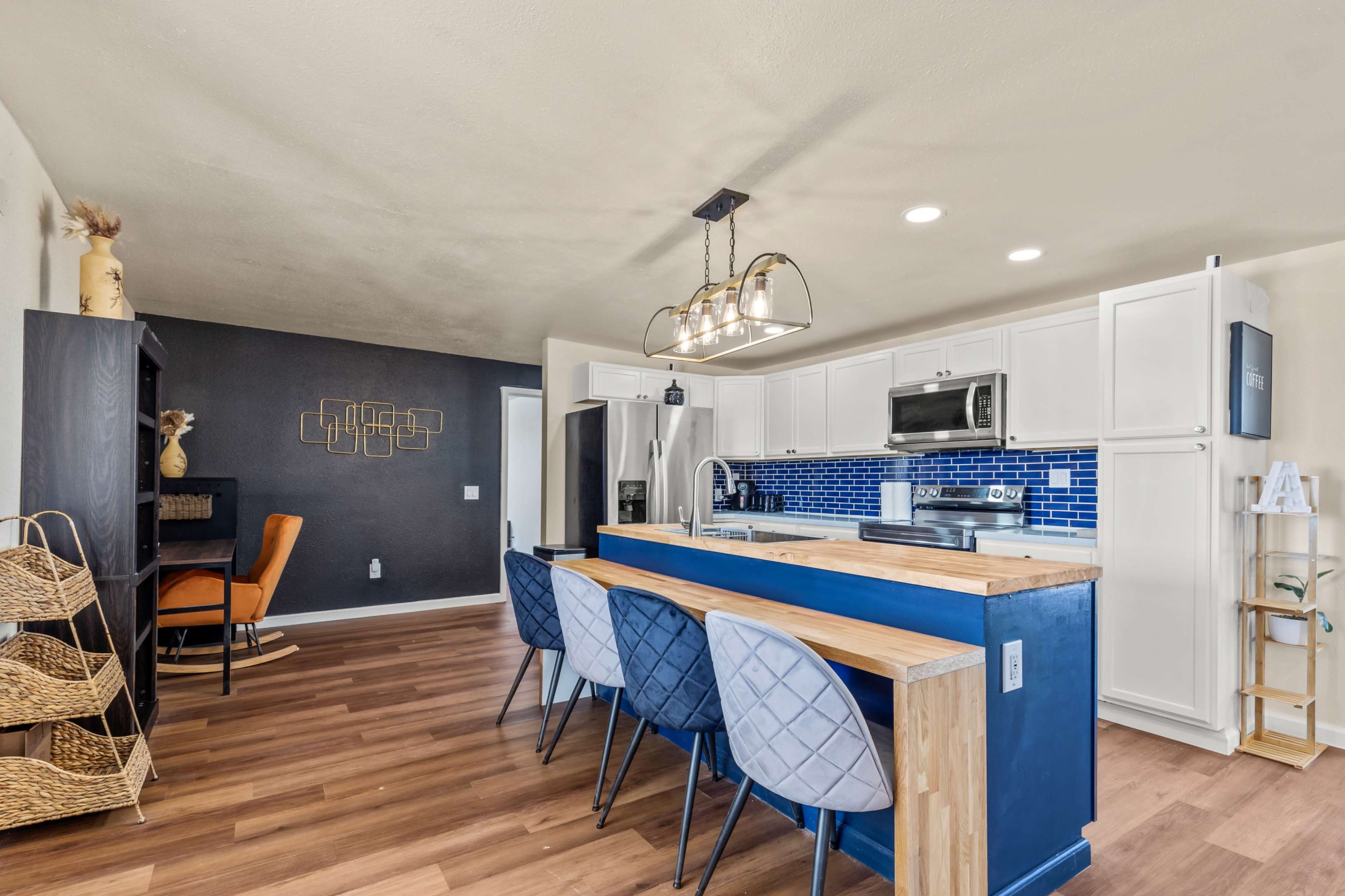 A modern kitchen with white cabinets, a blue accent wall, and a wooden island with four blue chairs.