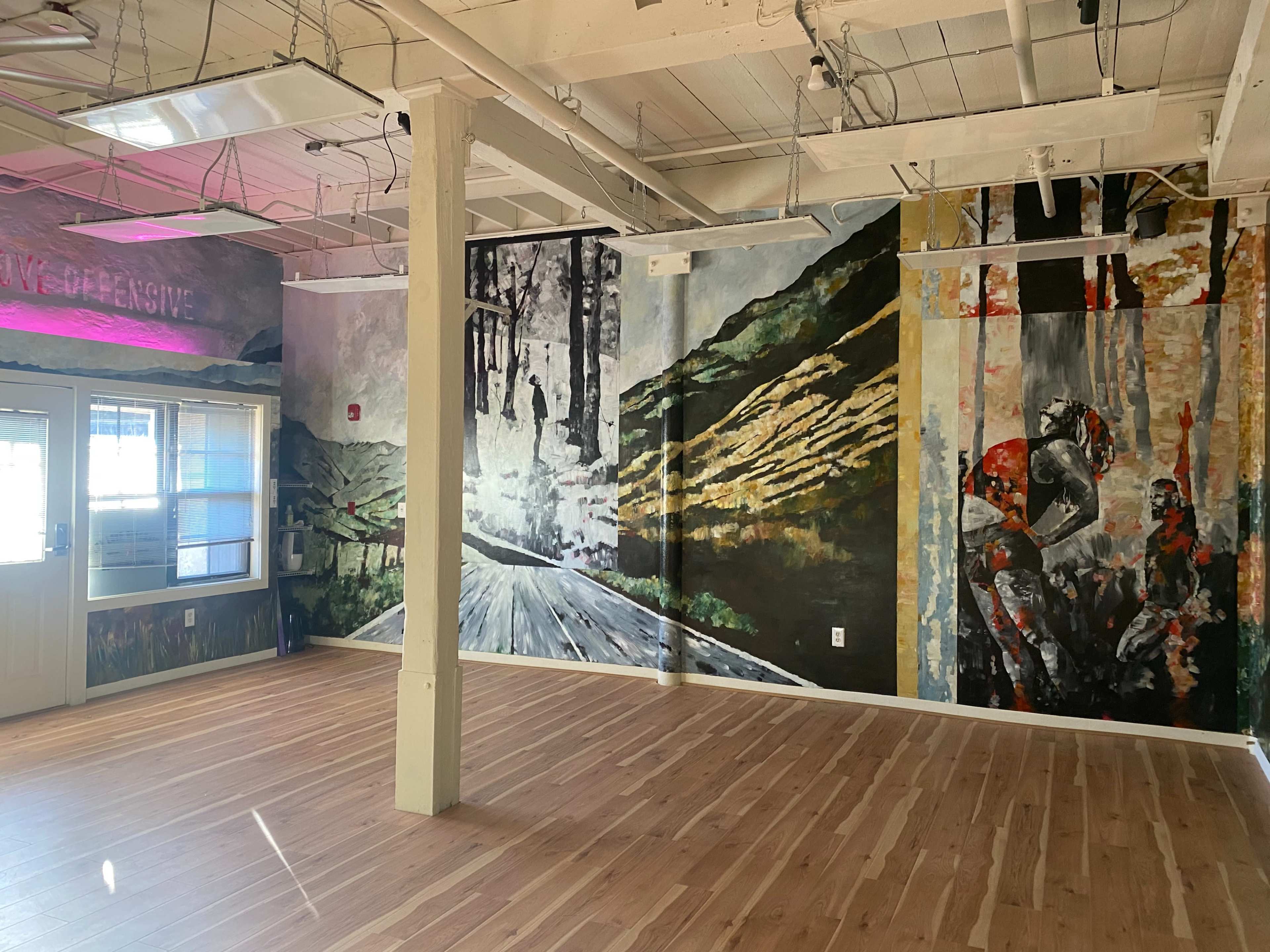 An interior space featuring large, colorful murals on the walls, with wooden flooring and ceiling beams visible.