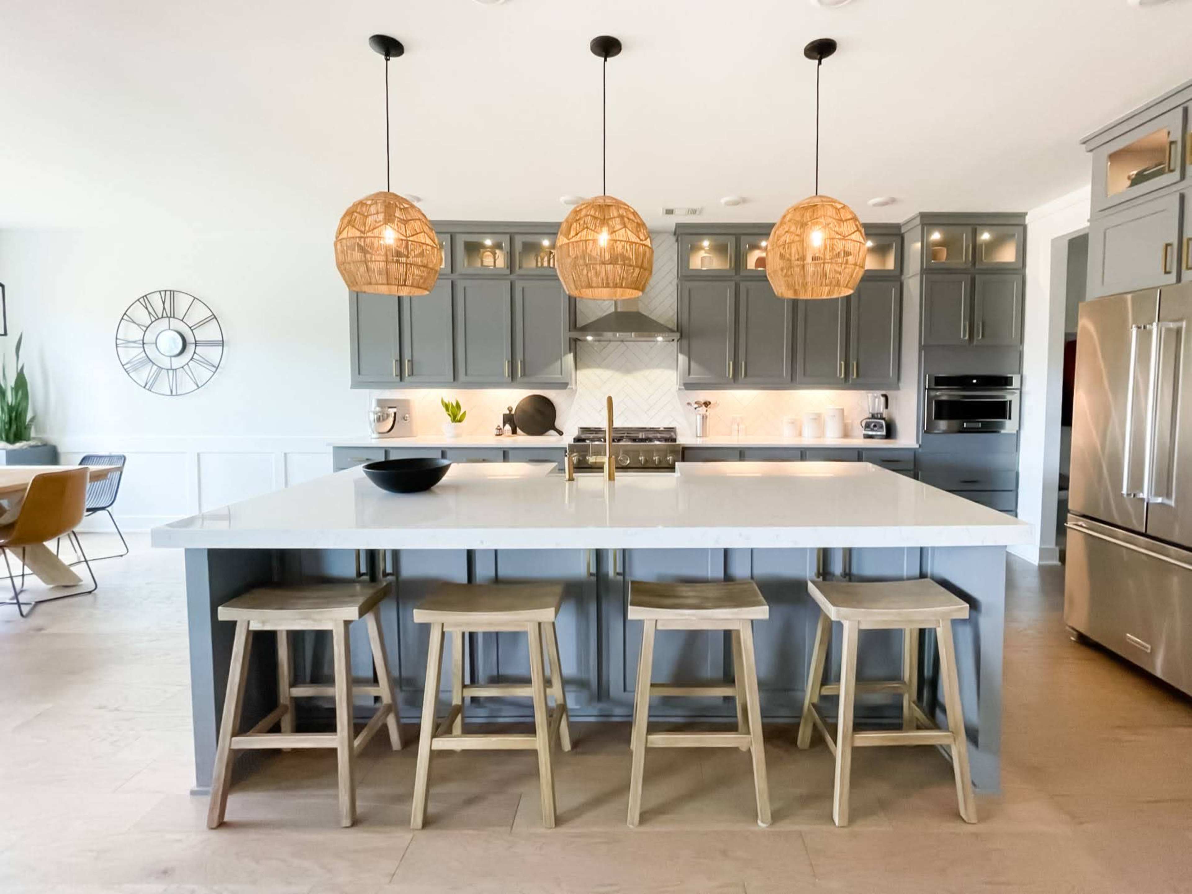 The kitchen features a large island with three pendant lights overhead, surrounded by wooden stools and modern cabinetry.