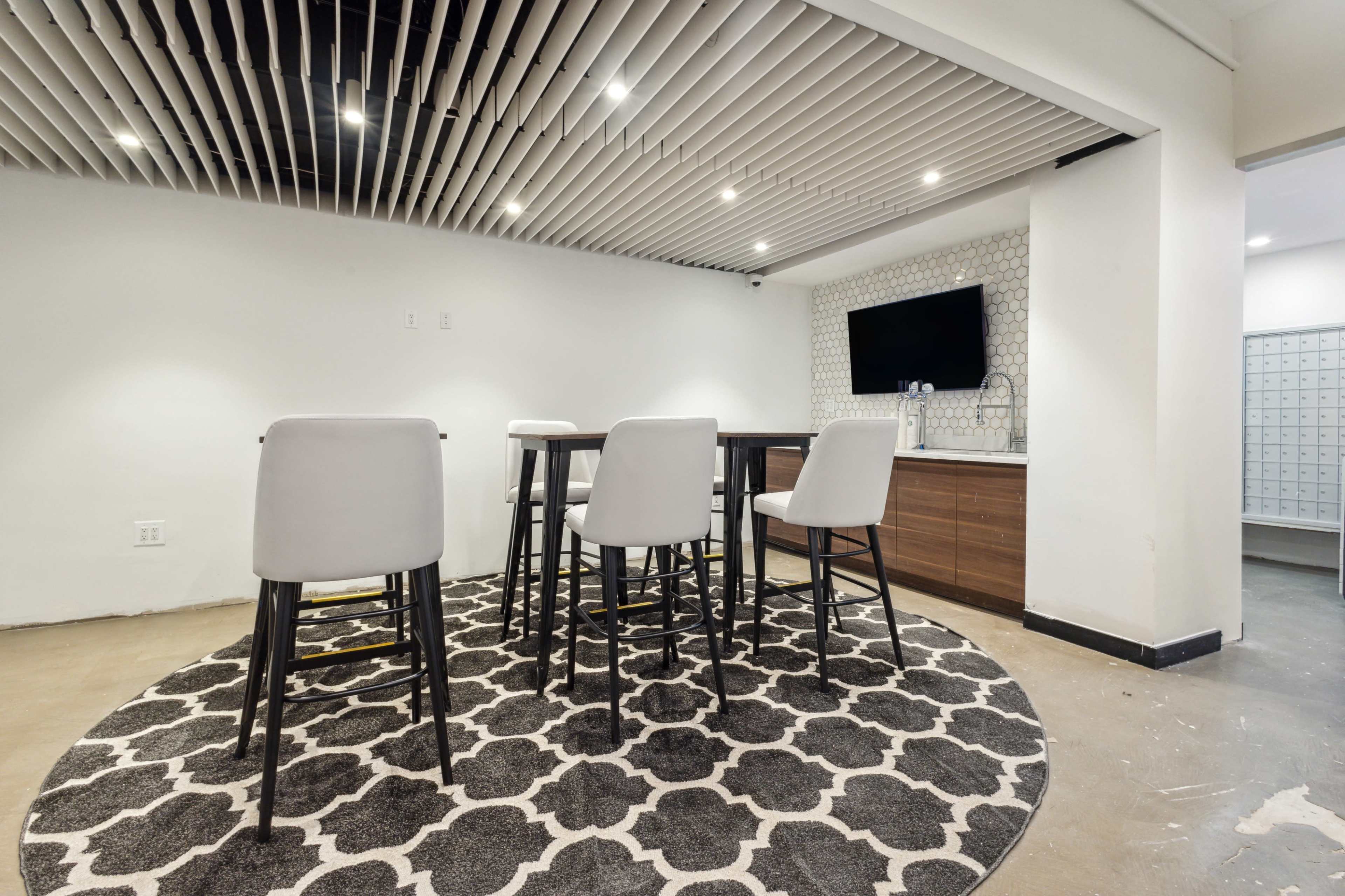 A modern room with a circular patterned rug, a table surrounded by four stools, and a wall-mounted television.