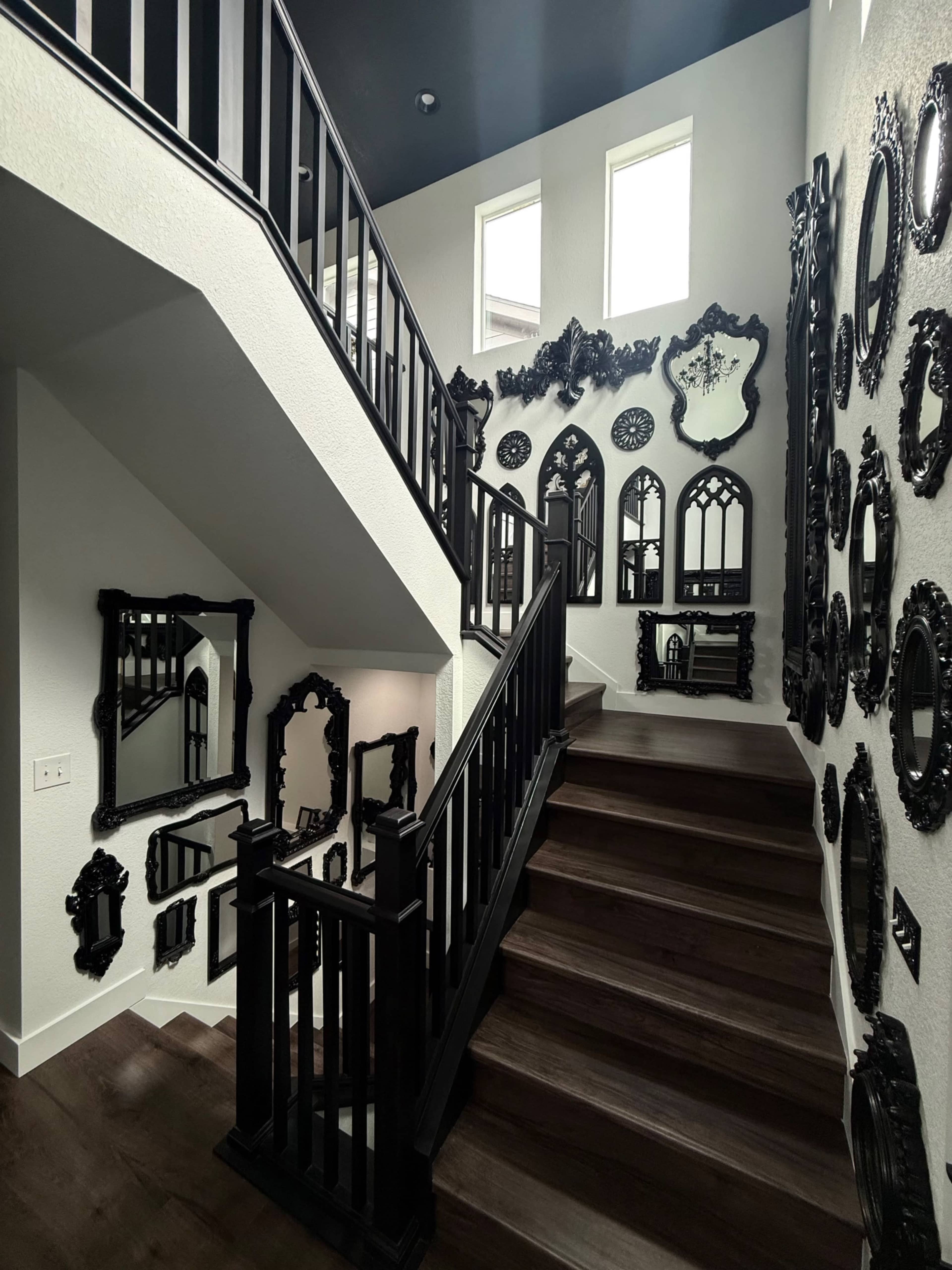 A staircase with dark wood steps and a black railing is flanked by a wall adorned with various ornate black mirrors.