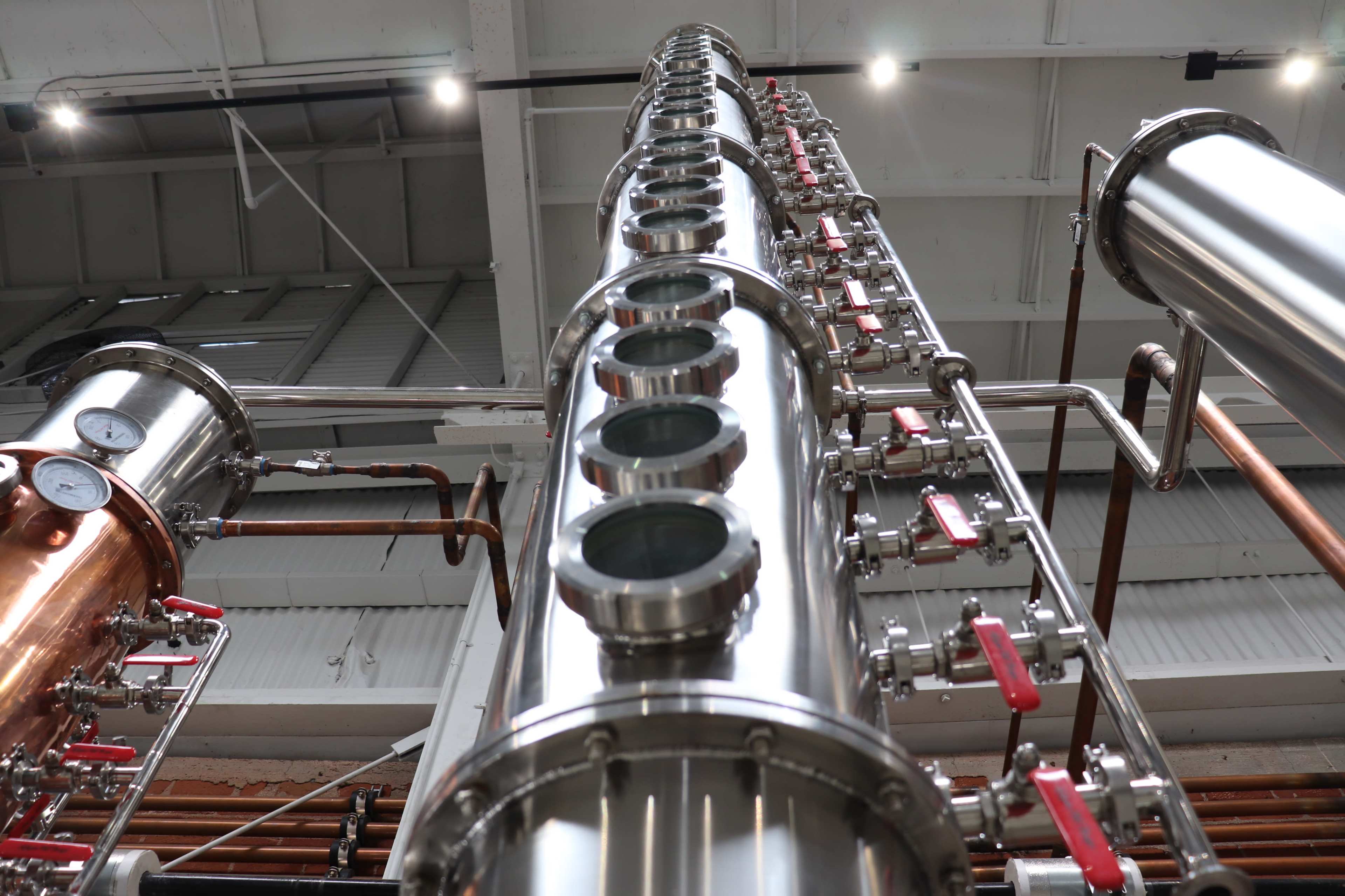 A vertical stainless steel distillation column equipped with multiple inspection windows and valves, set against a backdrop of a facility's interior.