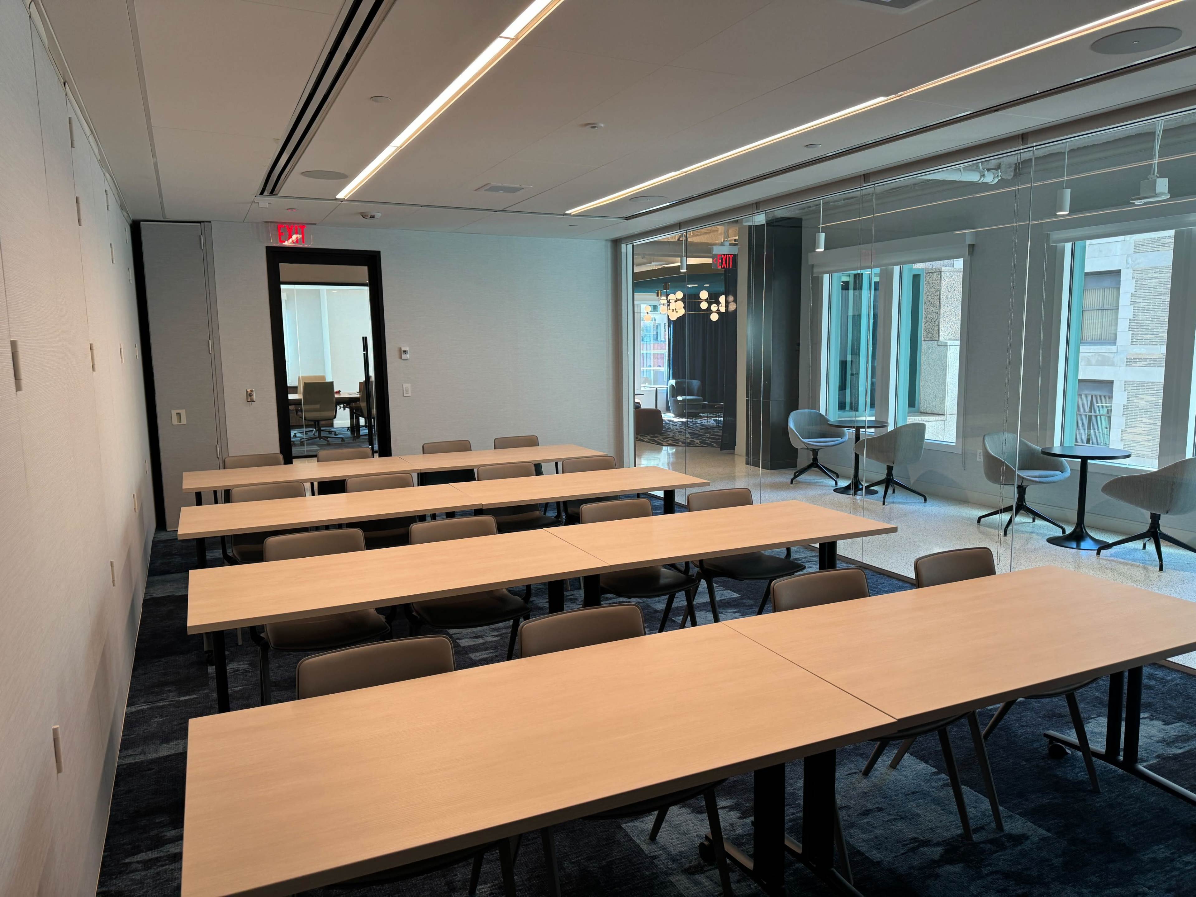 A modern conference room with several tables arranged in rows and large windows providing natural light.