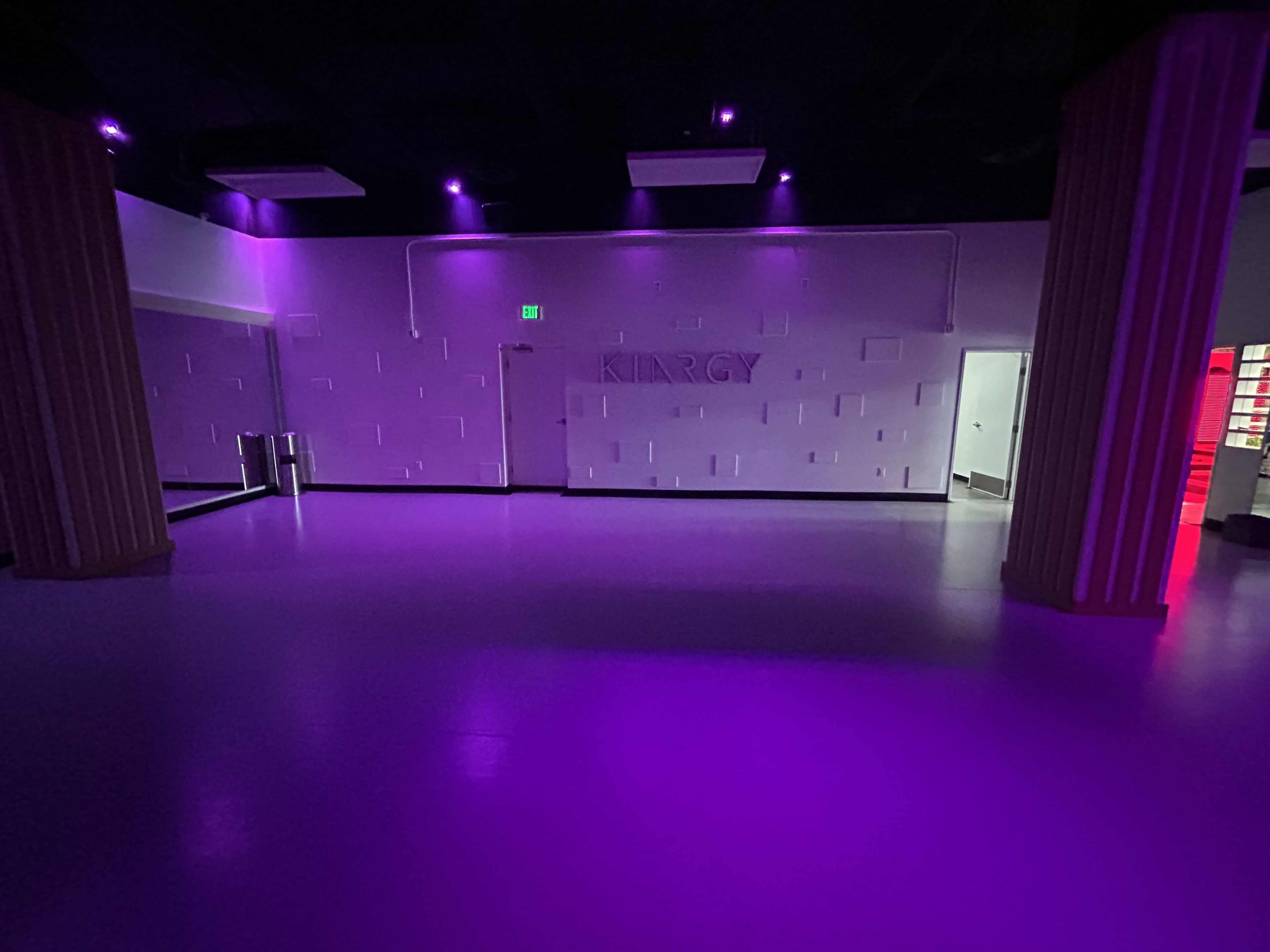 The image shows a dimly lit room with purple lighting, featuring a wall that displays the word "KIARGY" and a doorway on the right.