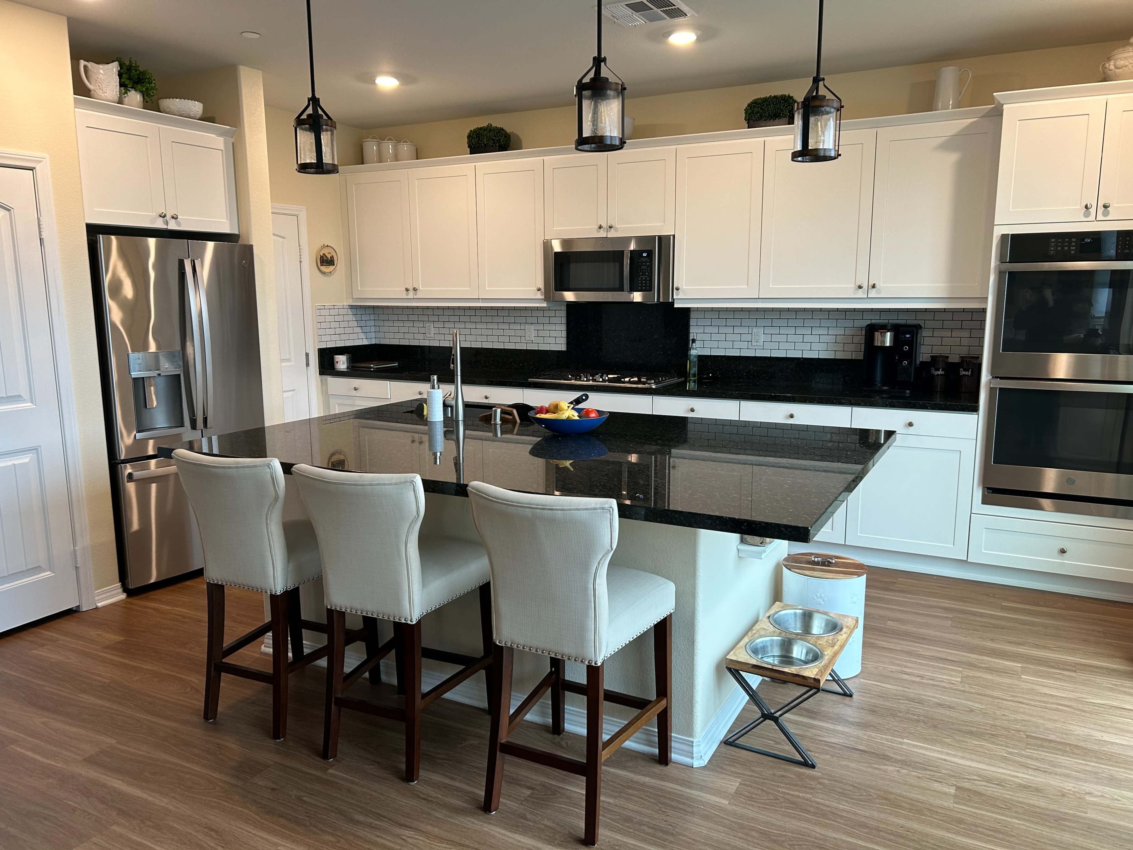 A modern kitchen with white cabinetry, a black granite island, and three upholstered stools.