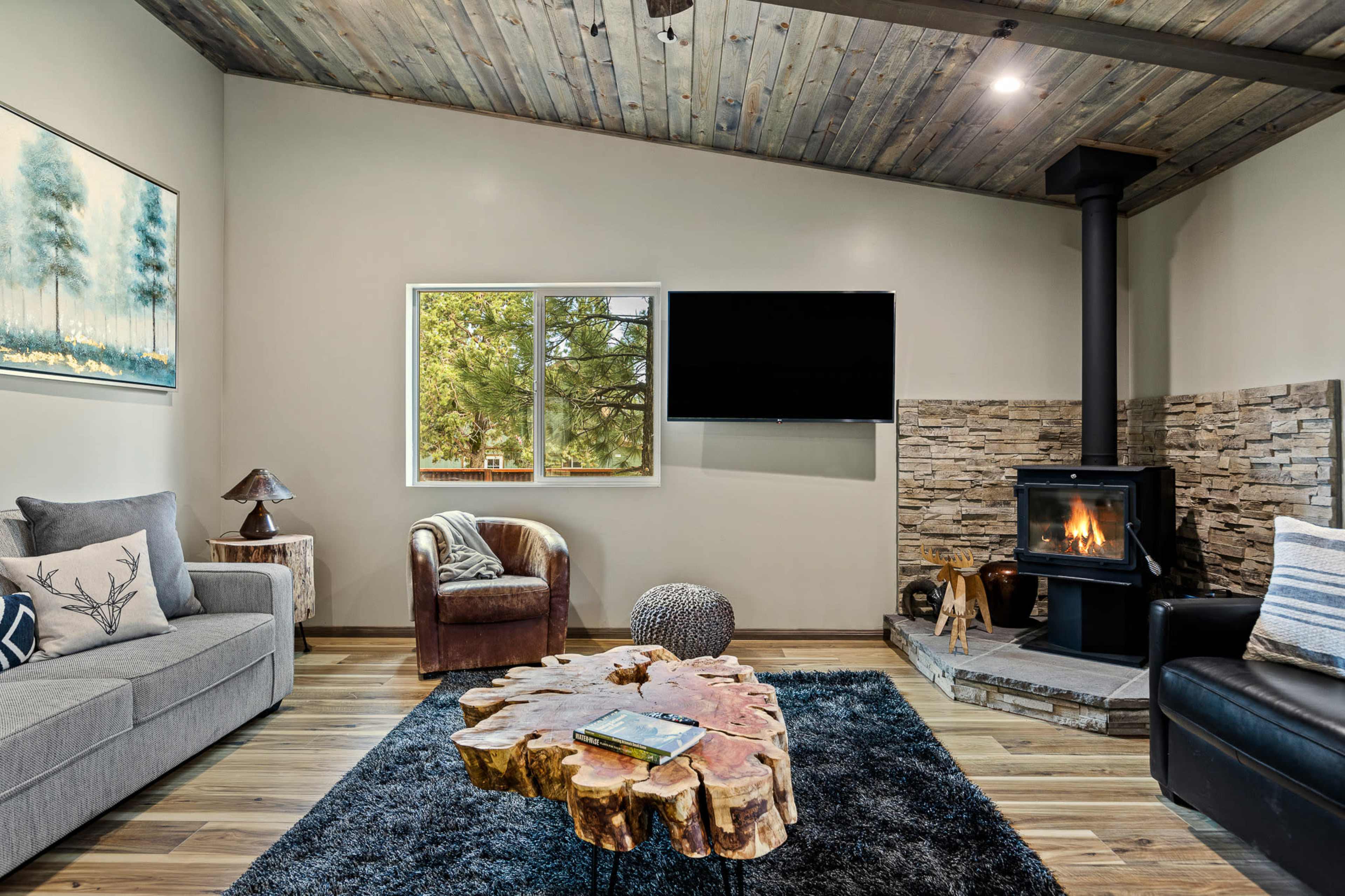 A living room features a sofa, an armchair, a stone fireplace, and a rustic wooden coffee table.