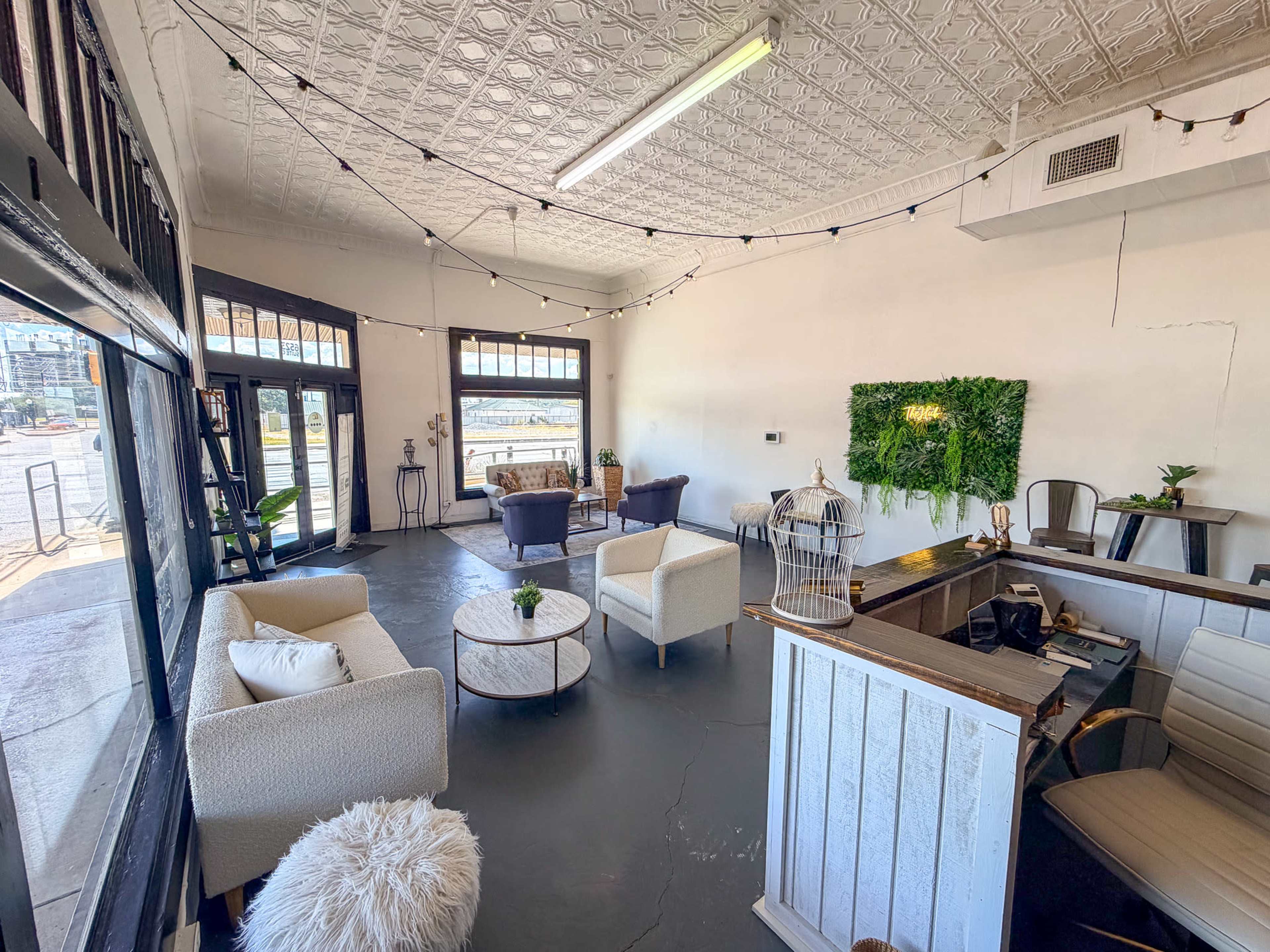 The image shows a well-lit, modern interior space with seating areas, plants, and a reception desk.