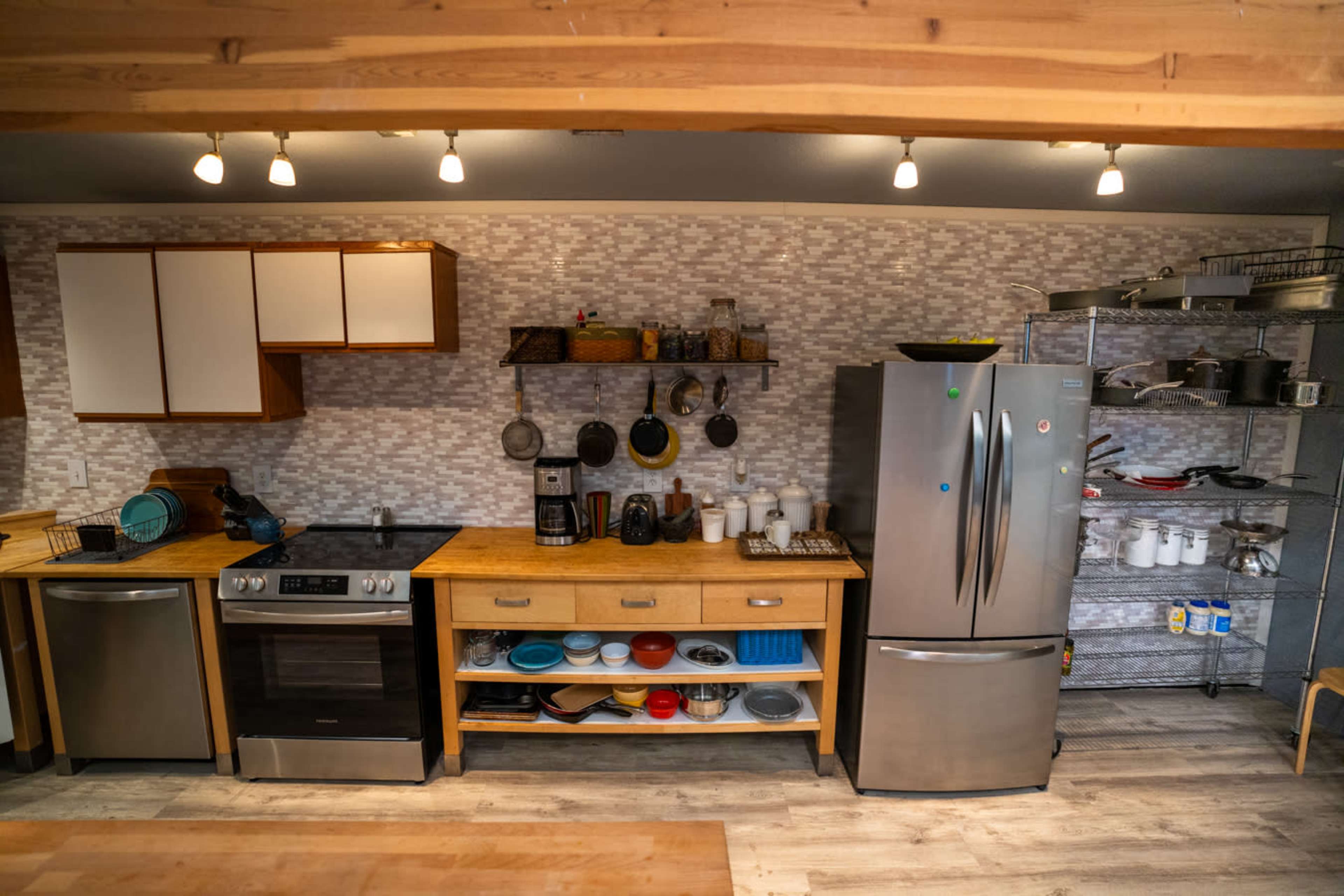 The image shows a modern kitchen with stainless steel appliances, wooden cabinetry, and organized shelving displaying various dishes and kitchen tools.