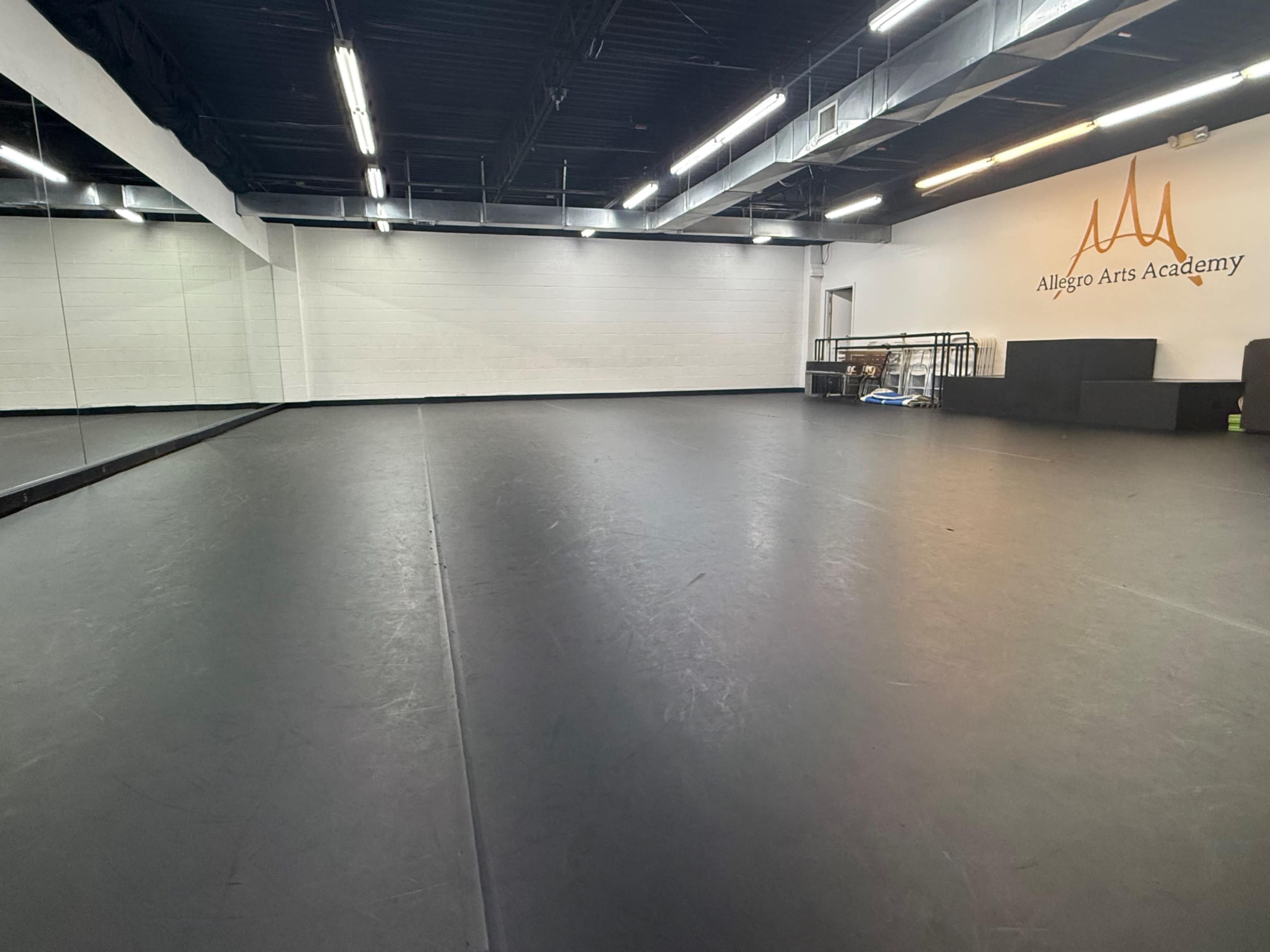 The image shows a spacious dance studio with a mirrored wall and a logo for Allegro Arts Academy on the side.