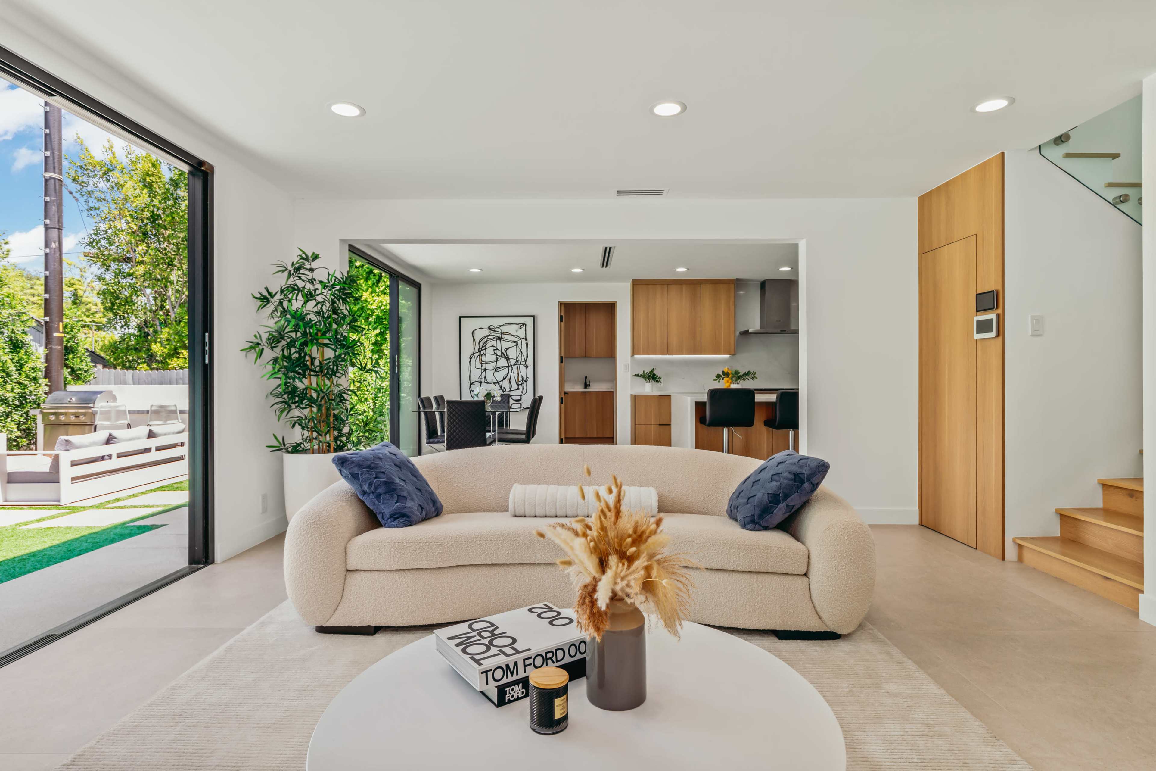 A modern living room features a beige sofa, a circular coffee table, and large glass doors leading to an outdoor space.