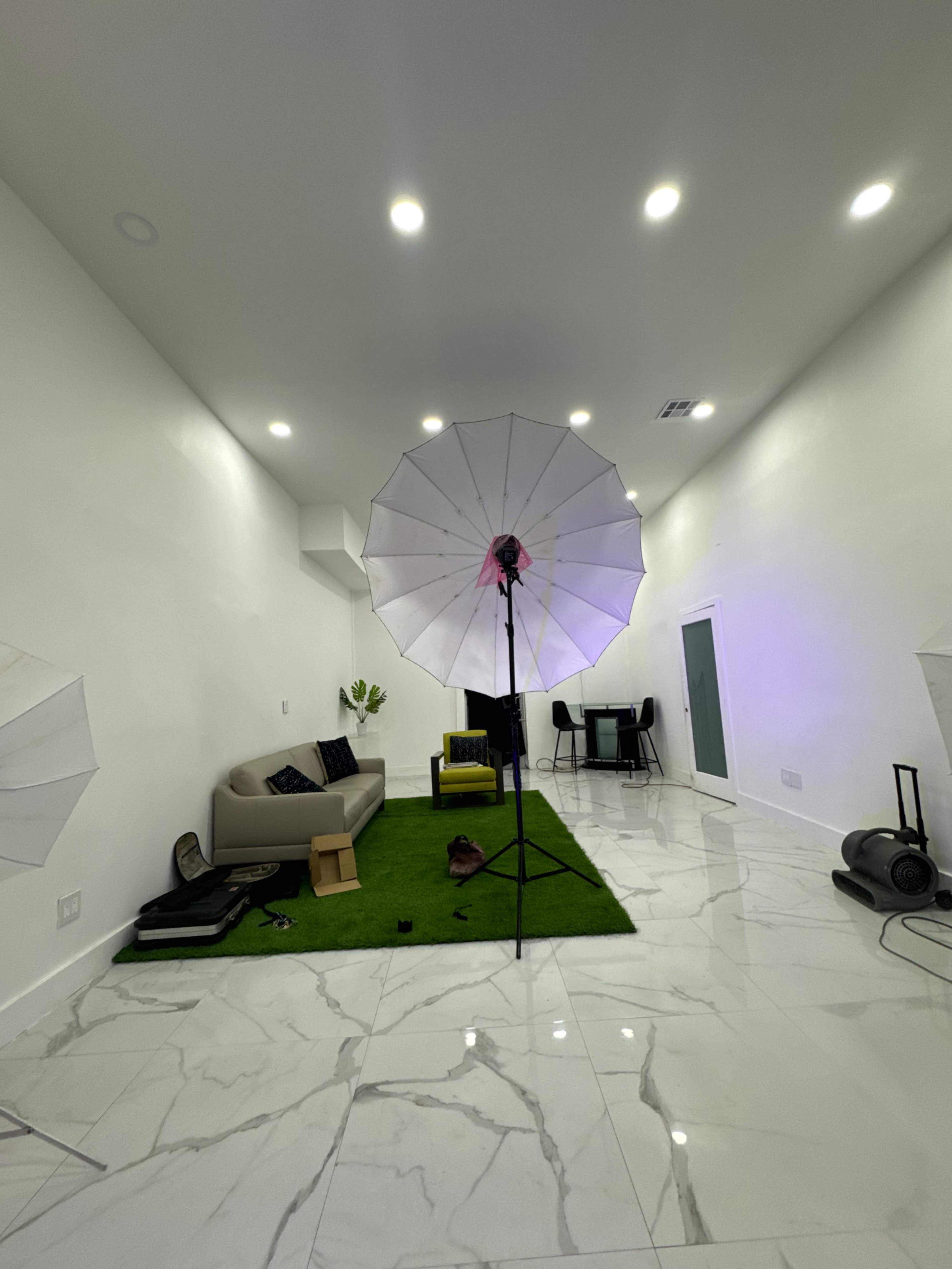 A spacious room with marble floors, two large light umbrellas set up, a green rug, a sofa, and a table in the background.