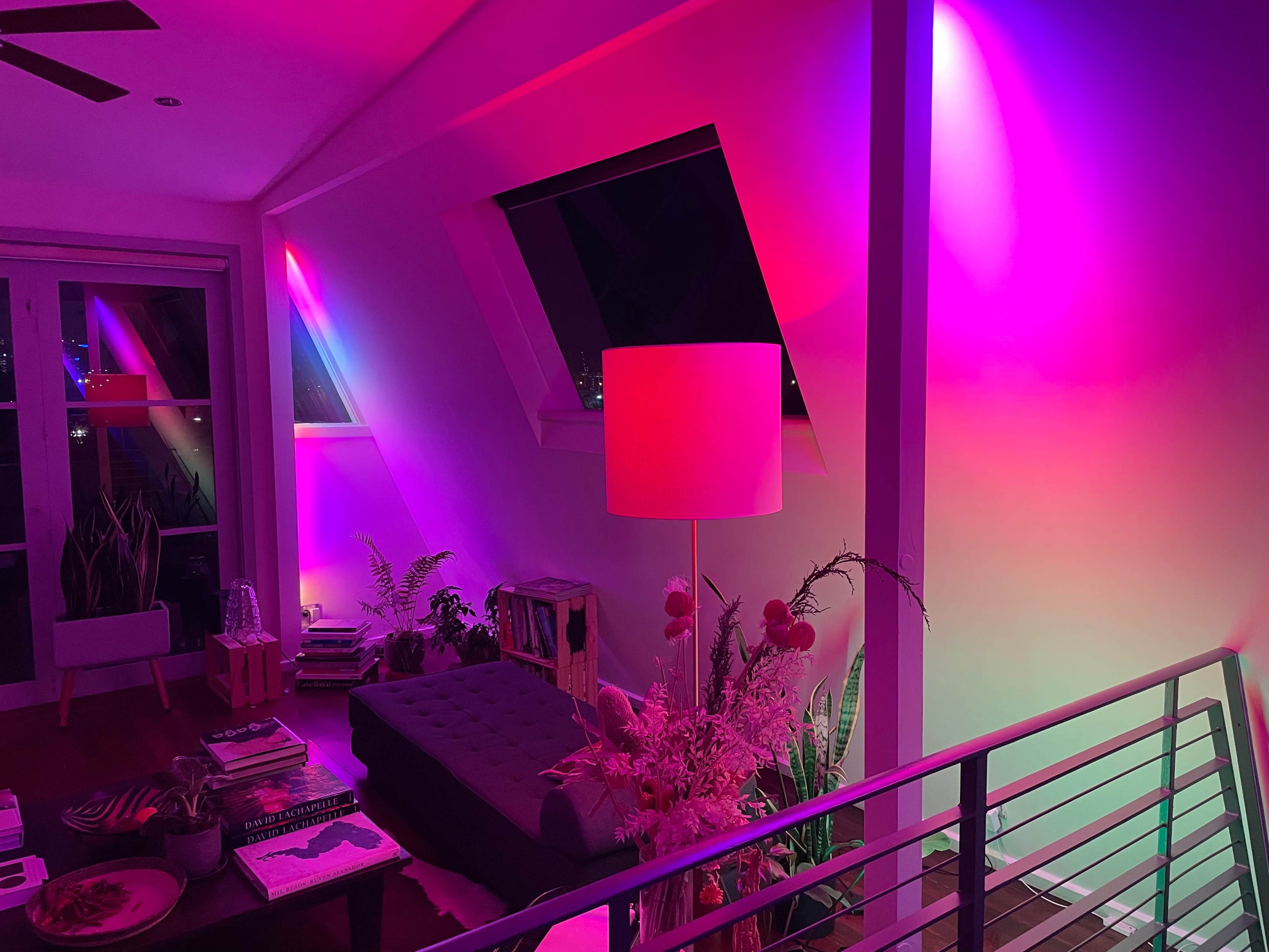 A modern living space features a sofa, a lamp, and vibrant pink and purple lights illuminating the walls and ceiling.