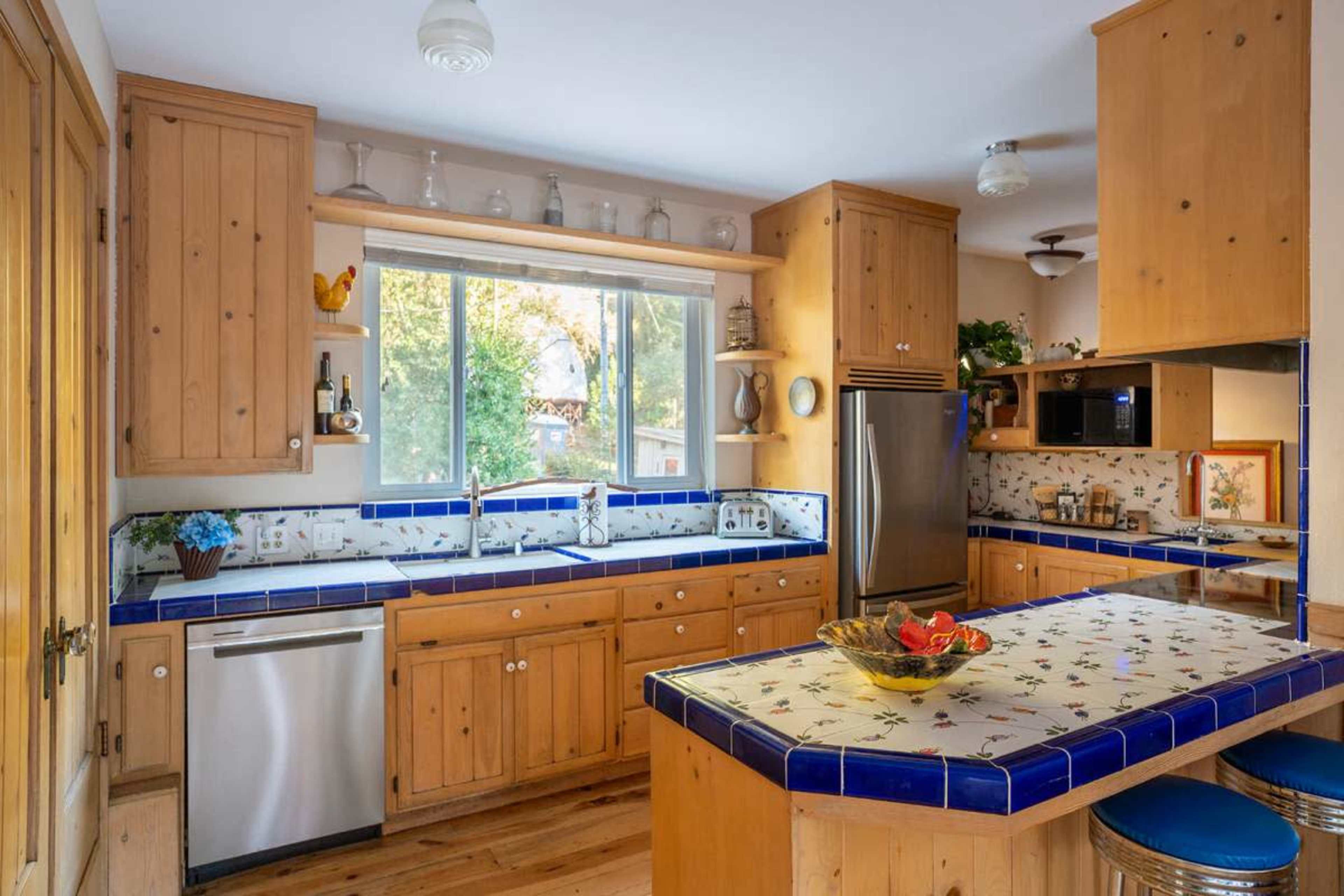 The kitchen features wooden cabinets, a blue-tiled countertop, and a large window that provides natural light.