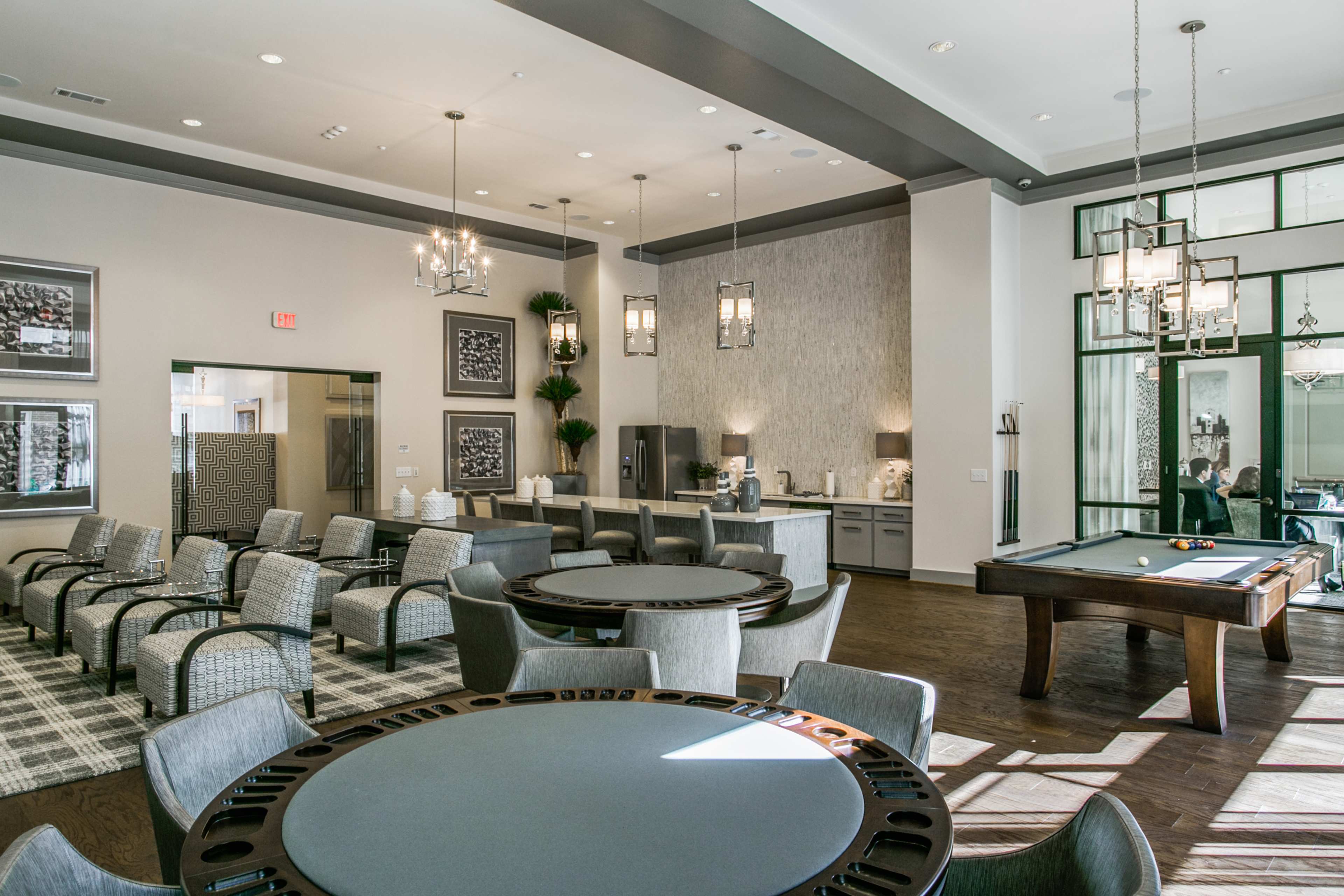 A modern lounge area featuring tables, chairs, and a pool table, with large windows allowing natural light to fill the space.