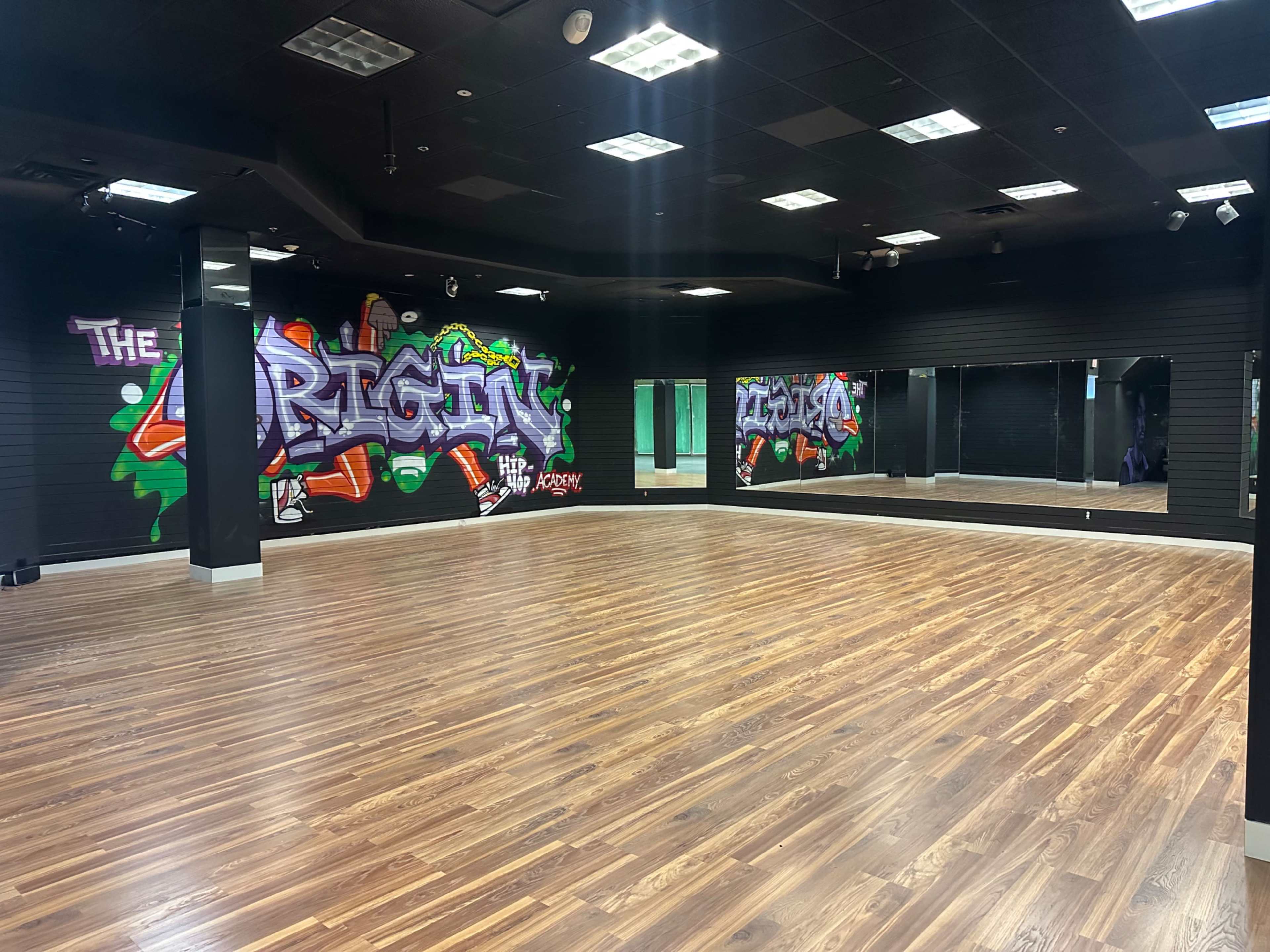 The image shows a spacious dance studio featuring a mirrored wall and vibrant graffiti art on one side.
