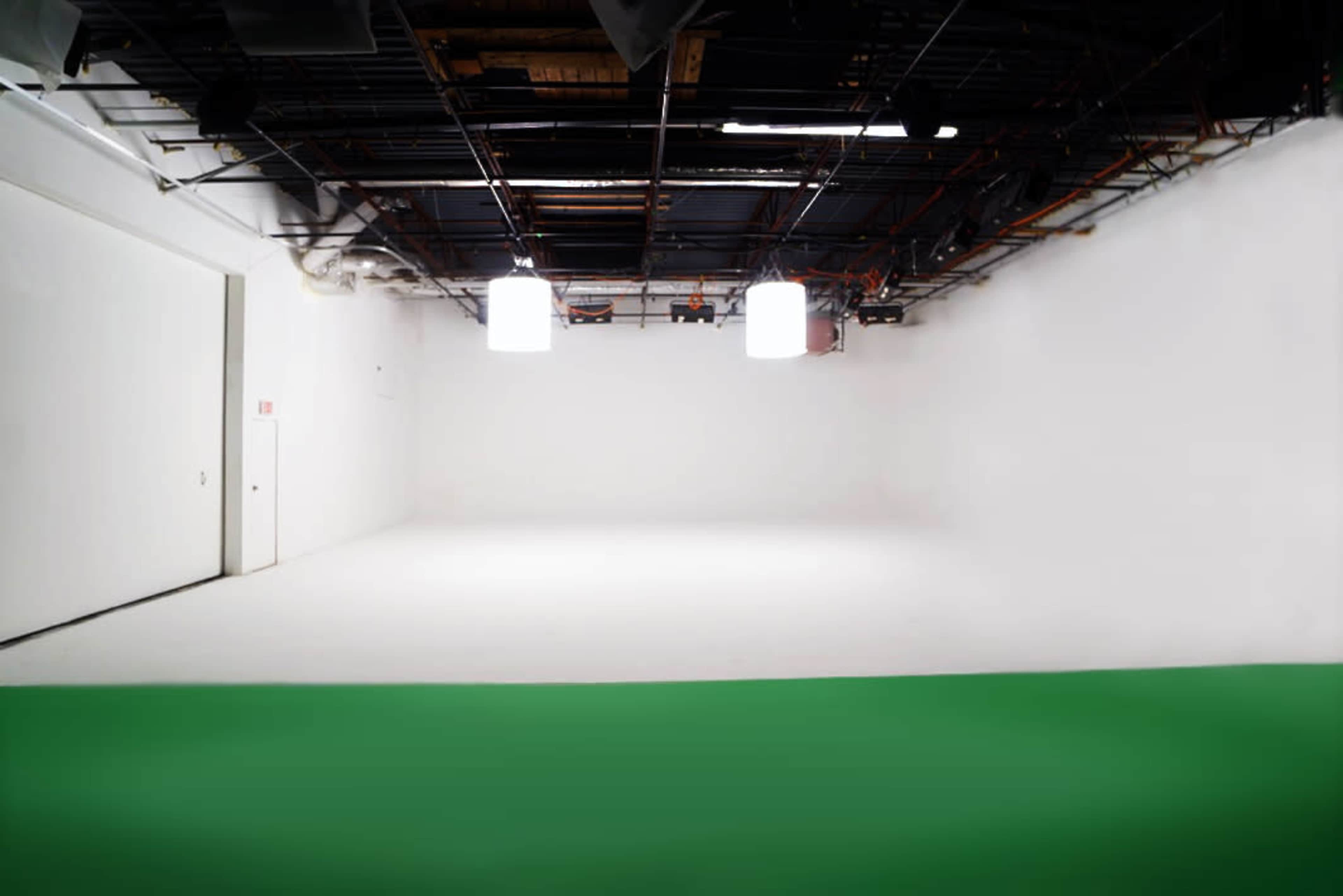A large, empty studio space features white walls and a green floor, with overhead lighting fixtures visible.