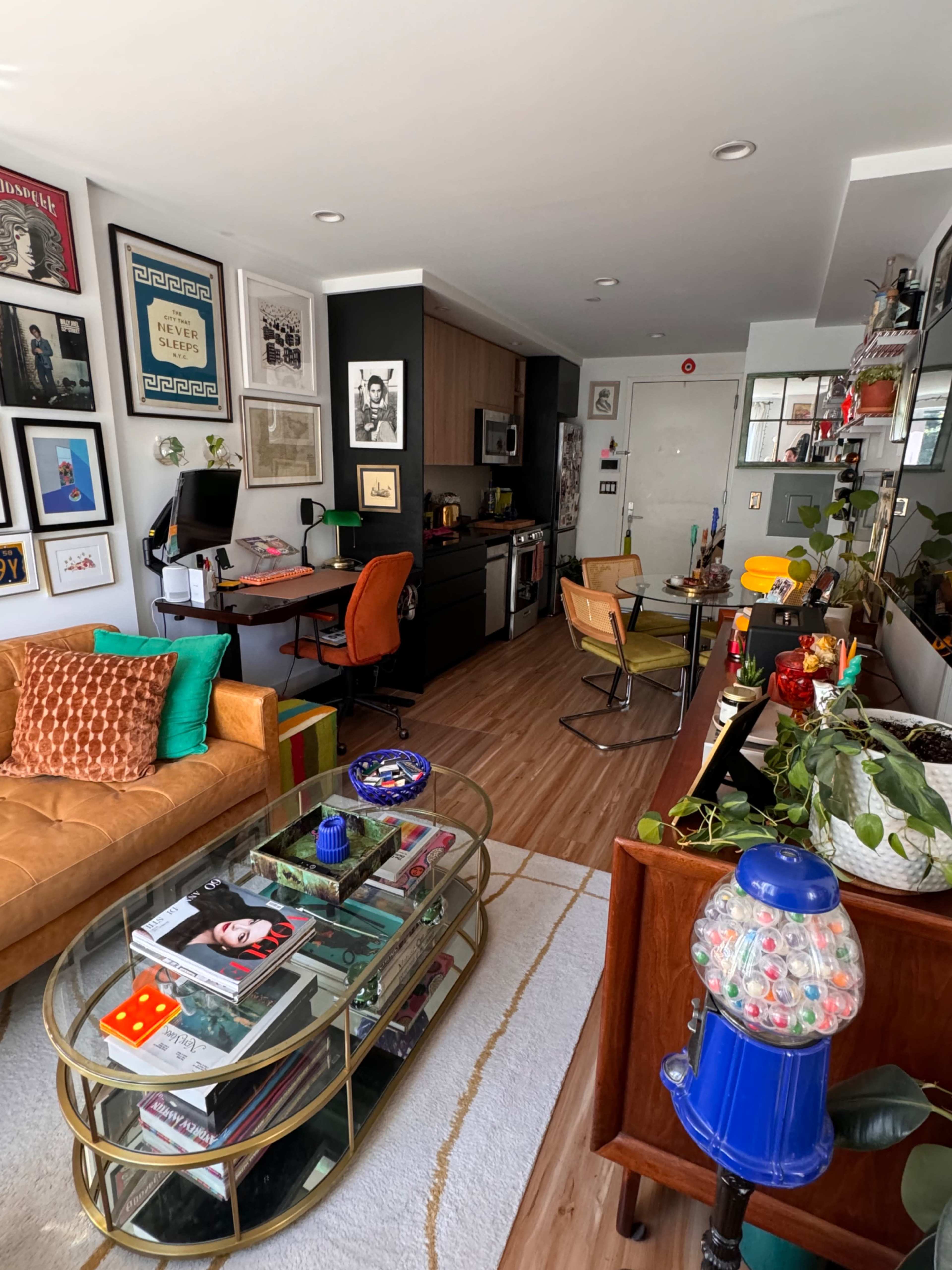 The image shows a modern living space with a mix of furniture, including a sofa, dining table, and various decorative art pieces on the walls.