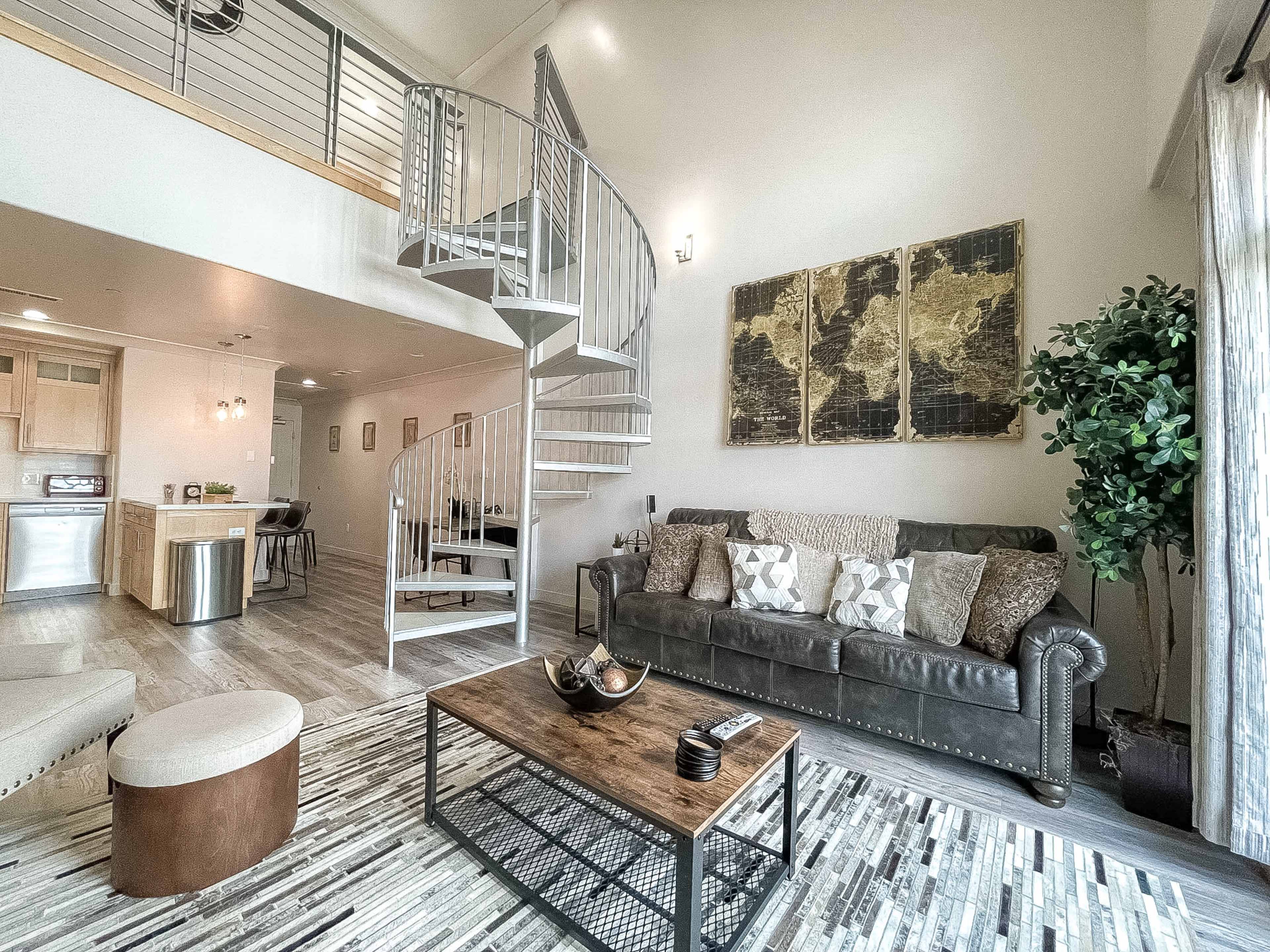 A modern living room featuring a leather sofa, a coffee table, and a spiral staircase leading to a loft area.