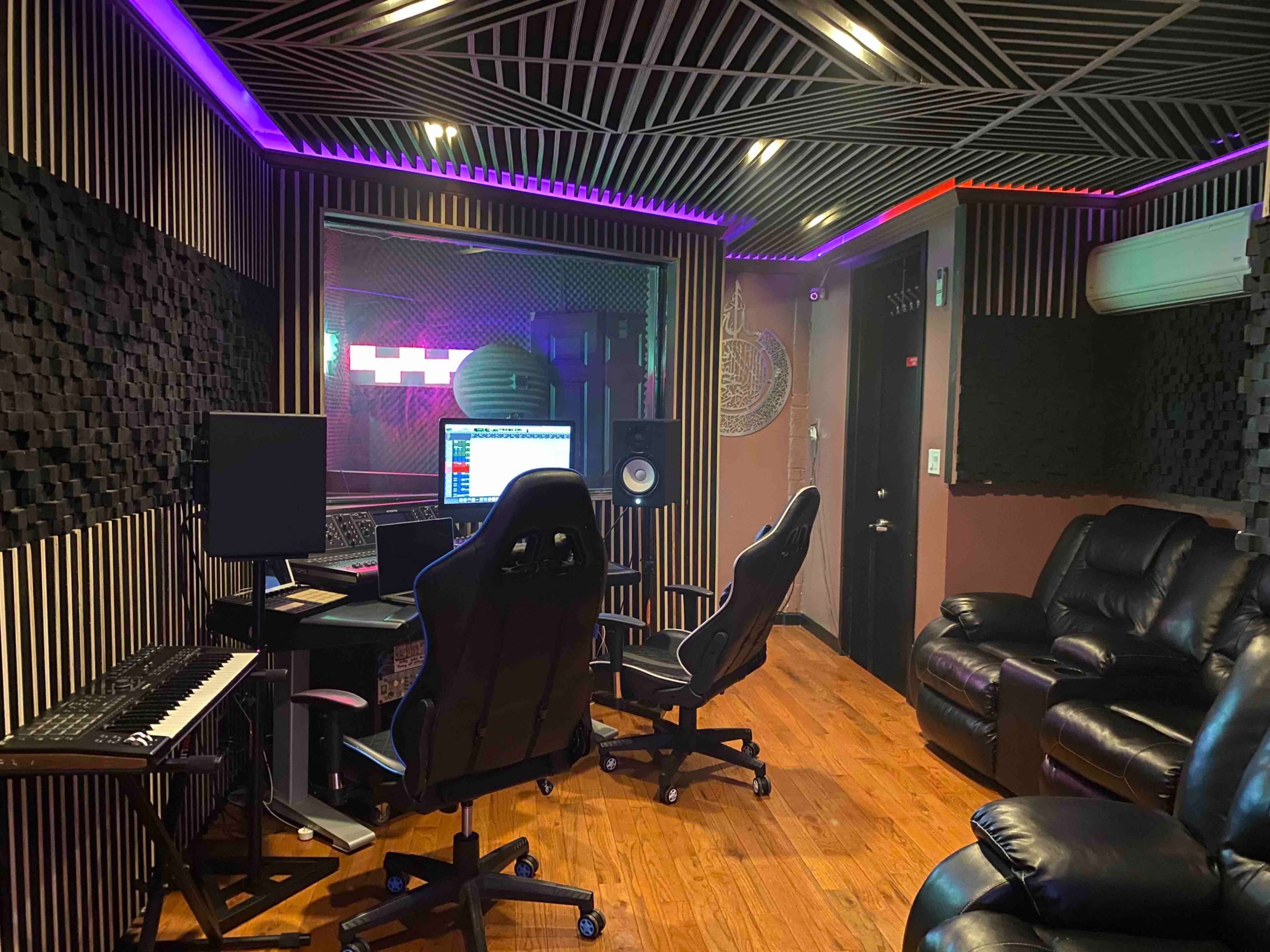 A music recording studio with a soundproof interior, featuring a mixing desk, computer monitors, and leather seating.