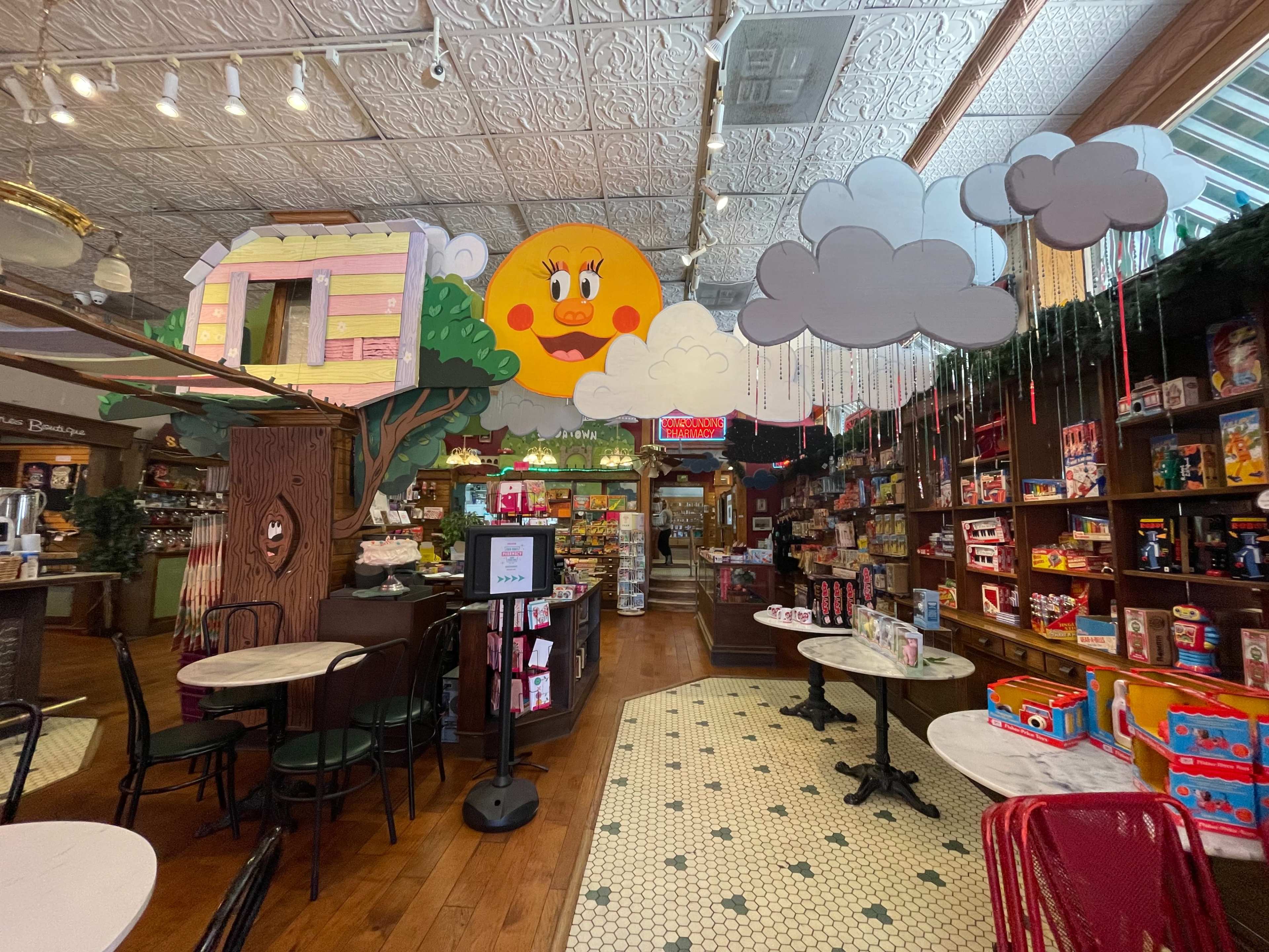 A colorful, whimsical interior of a candy store featuring decorative elements like a large sun, clouds, and various shelves filled with candy and snacks.
