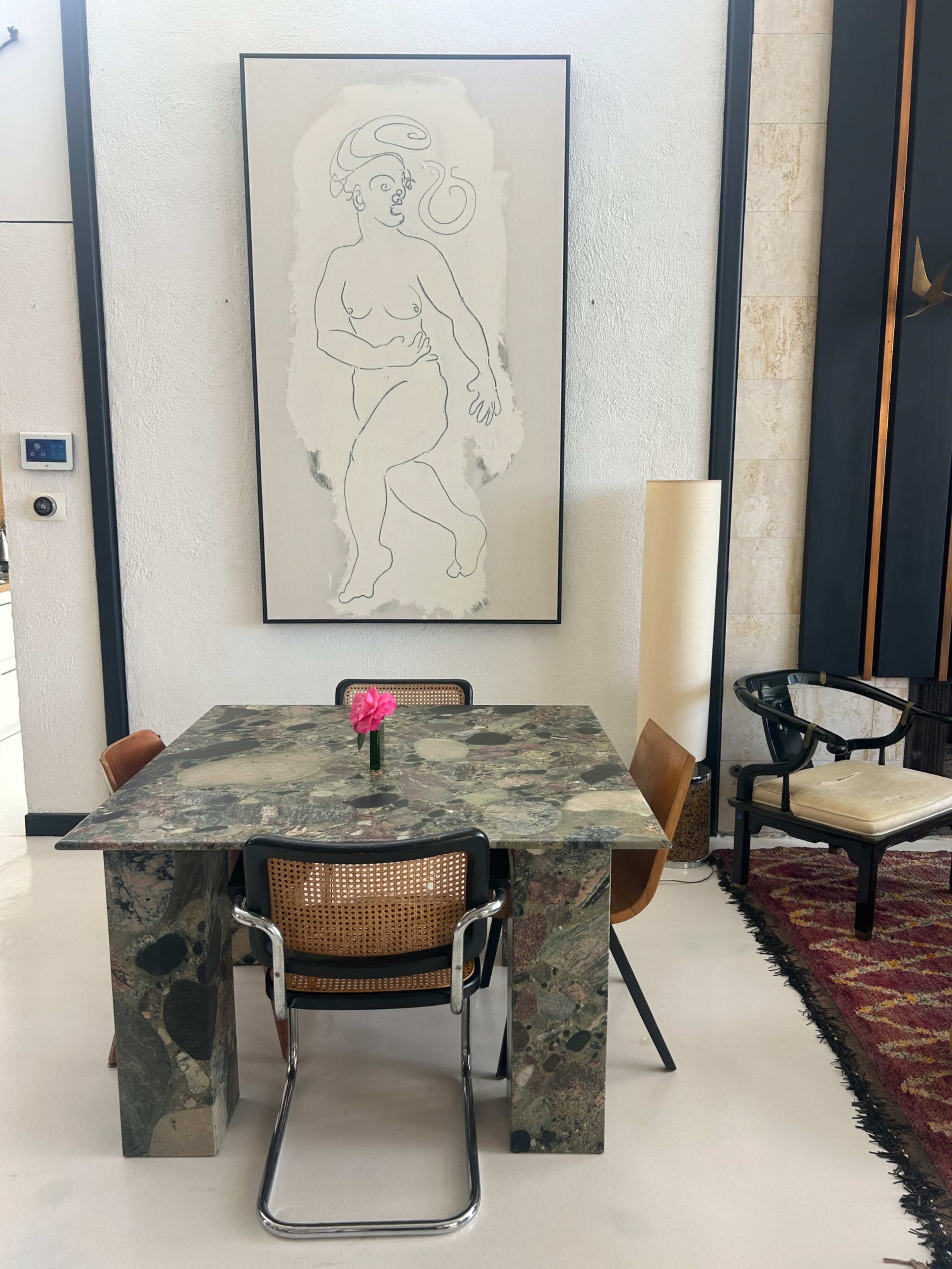 The image features a minimalist dining area with a marble table, four chairs, a flower vase, and a large framed artwork on the wall.