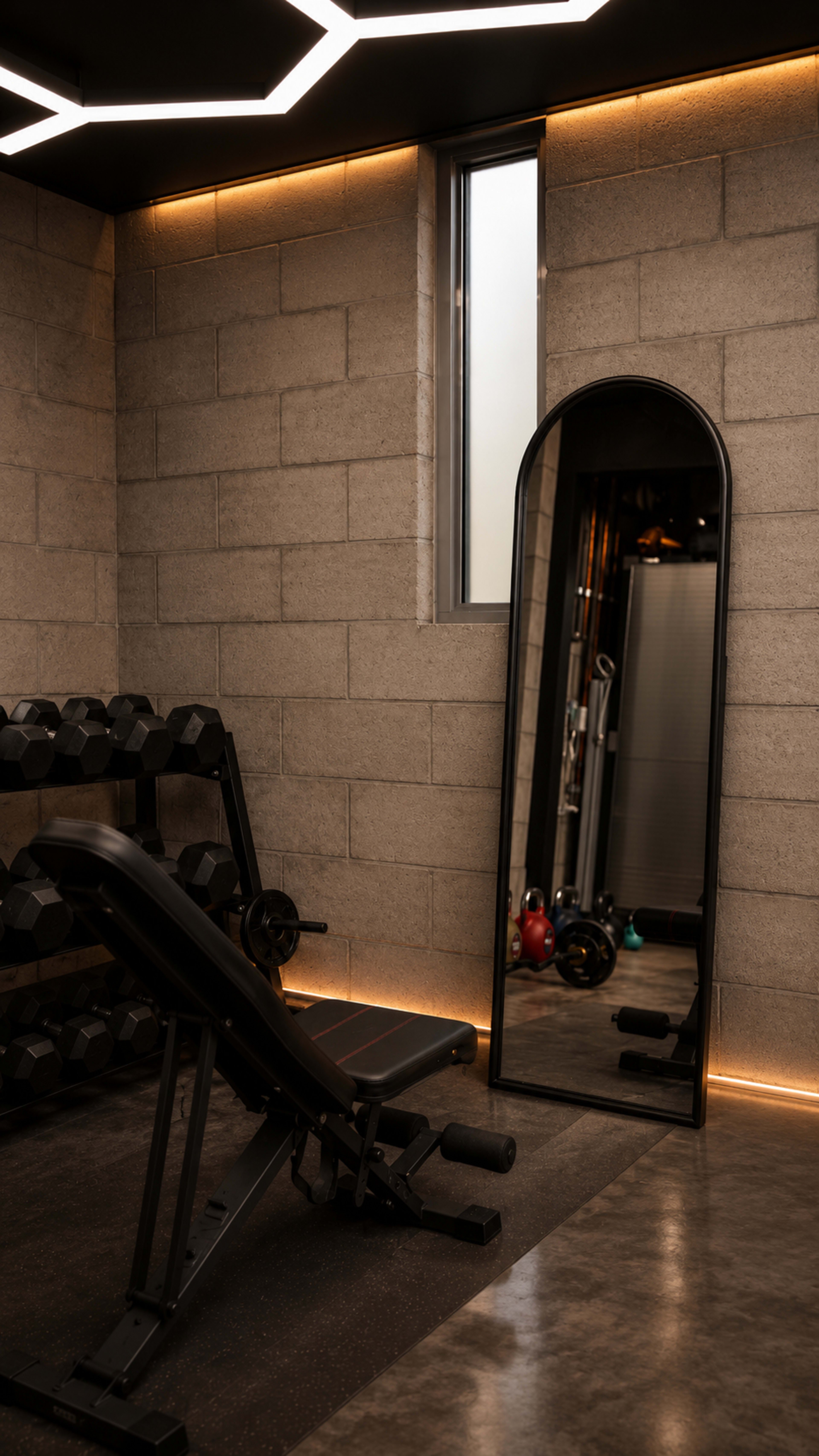 The image shows a minimalist gym interior with a weight bench, a set of dumbbells, and a tall mirror next to a window.