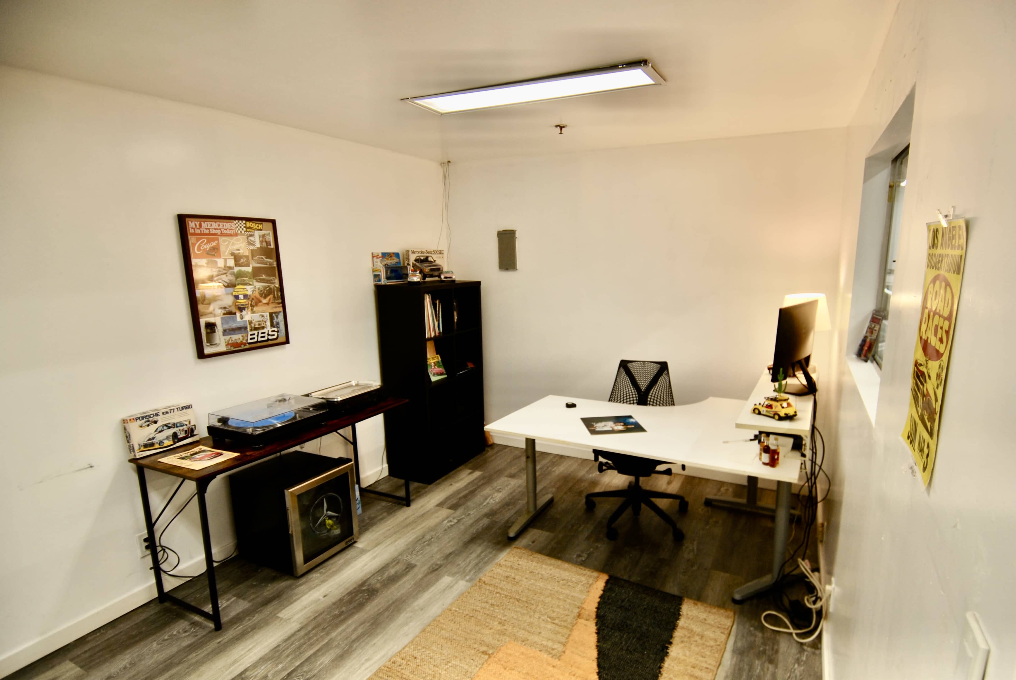 The image shows a minimalistic office space with a desk, a bookshelf, and a turntable on a side table.