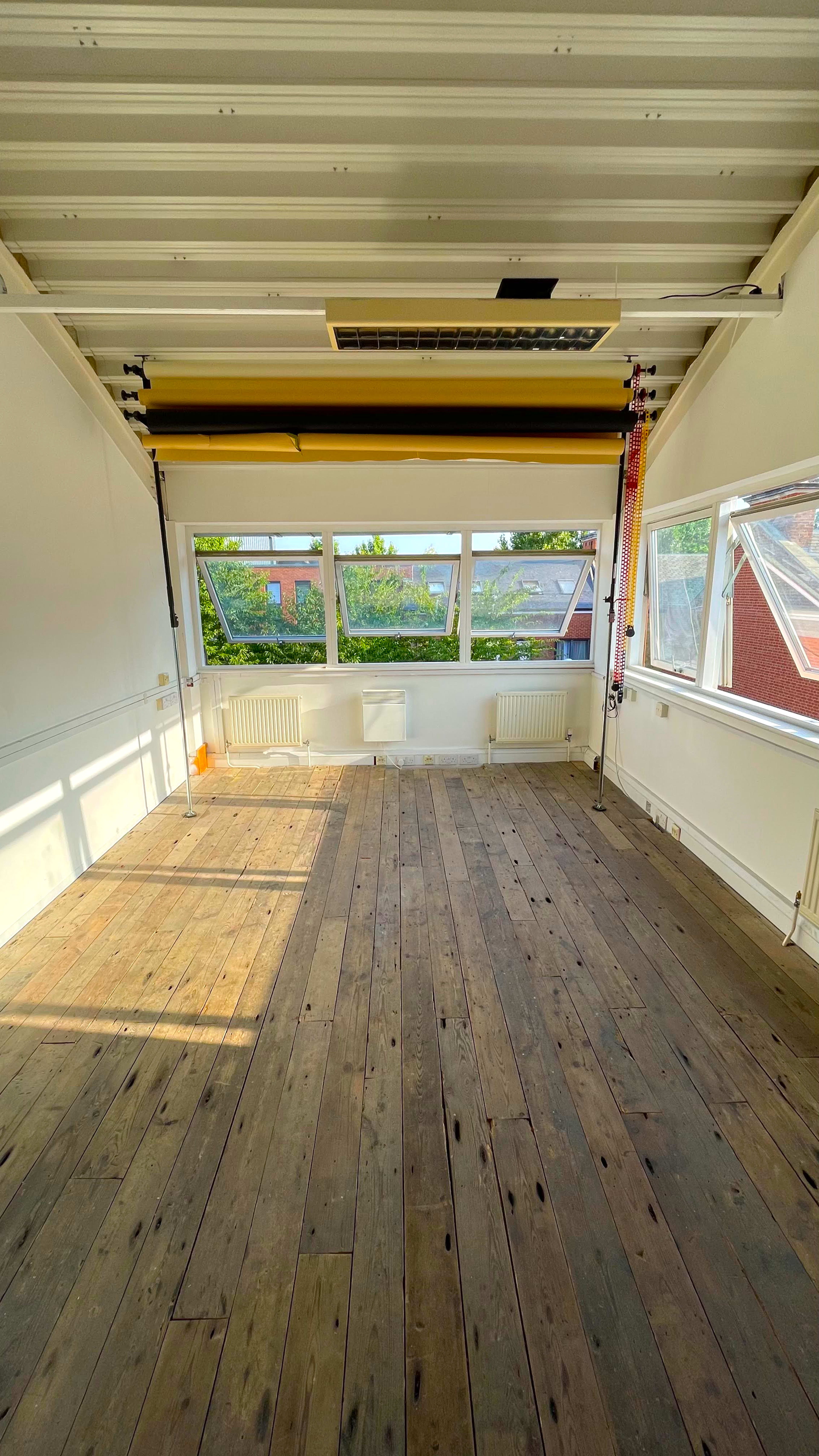 An empty room with wooden floors and large windows displaying a view of the outdoors.