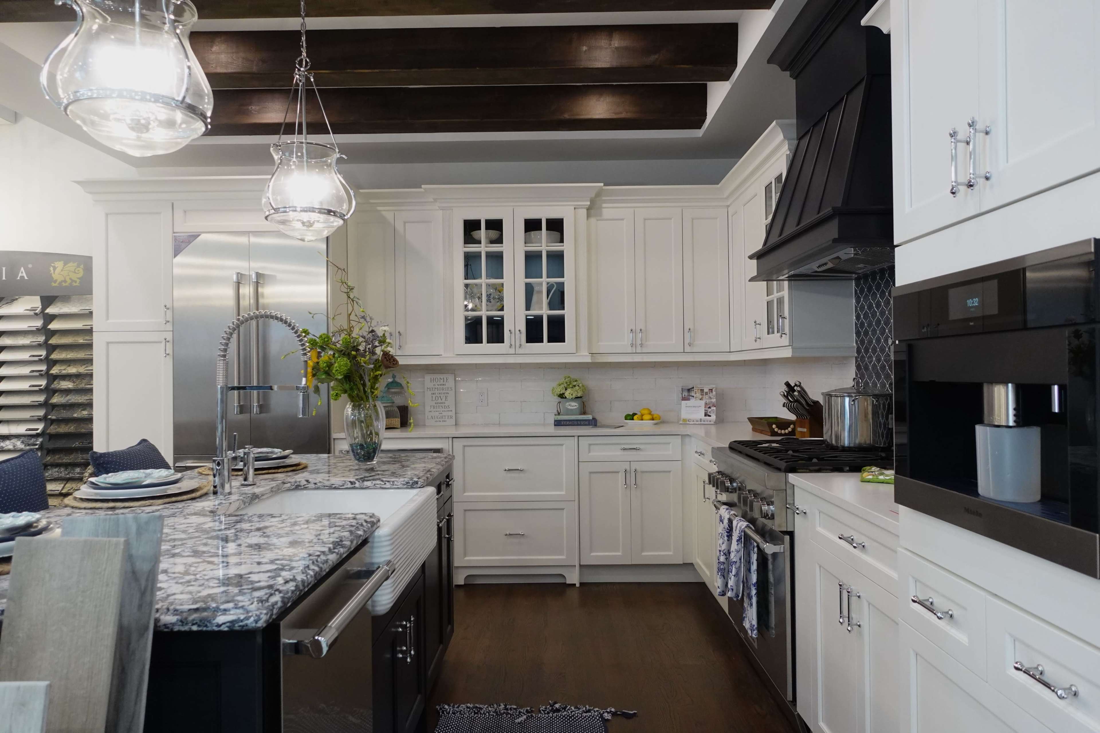 A modern kitchen featuring white cabinetry, a granite island, stainless steel appliances, and pendant lighting.