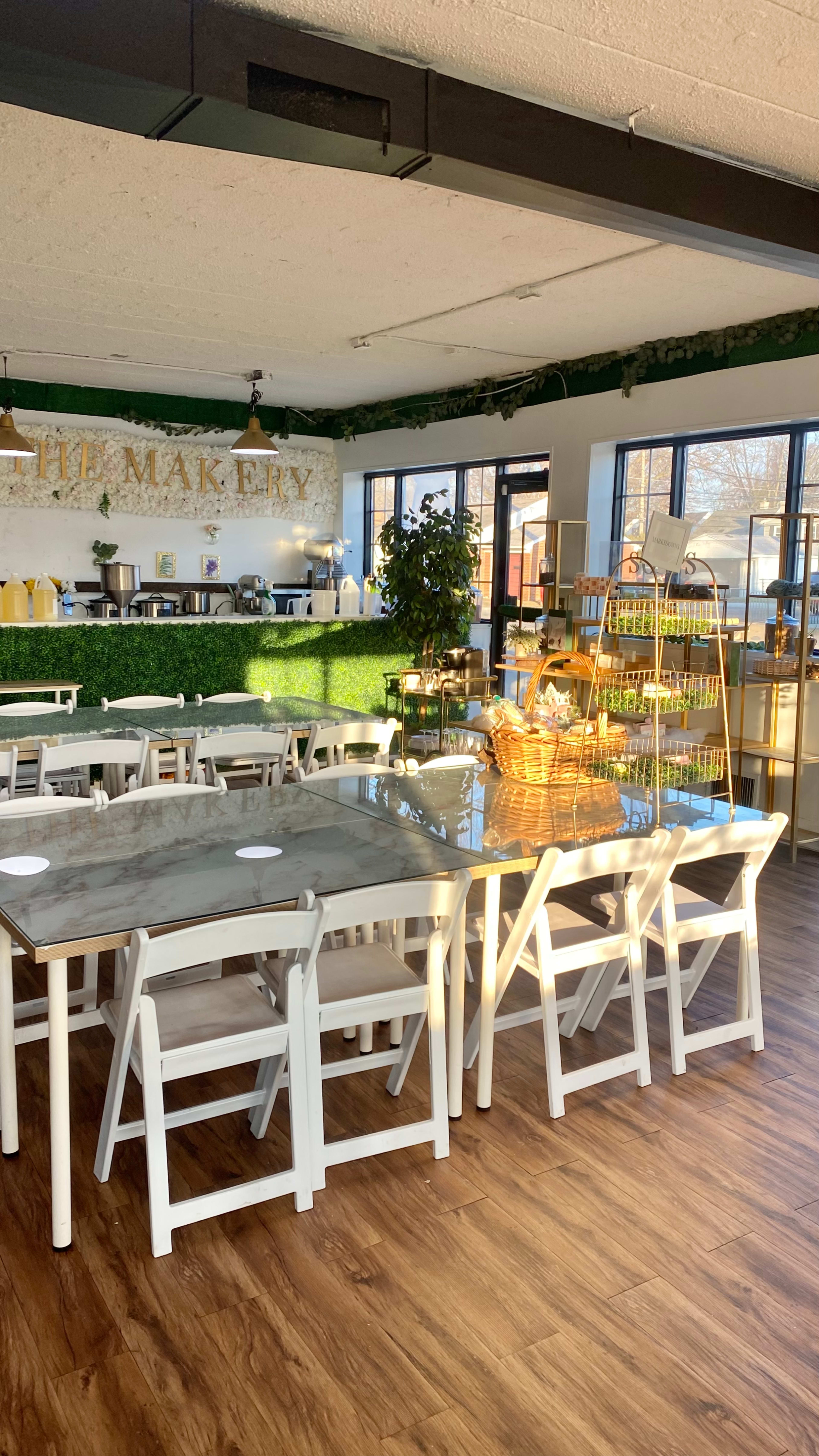 A bright café interior filled with white tables and chairs, featuring a green wall and a food display area in the background.