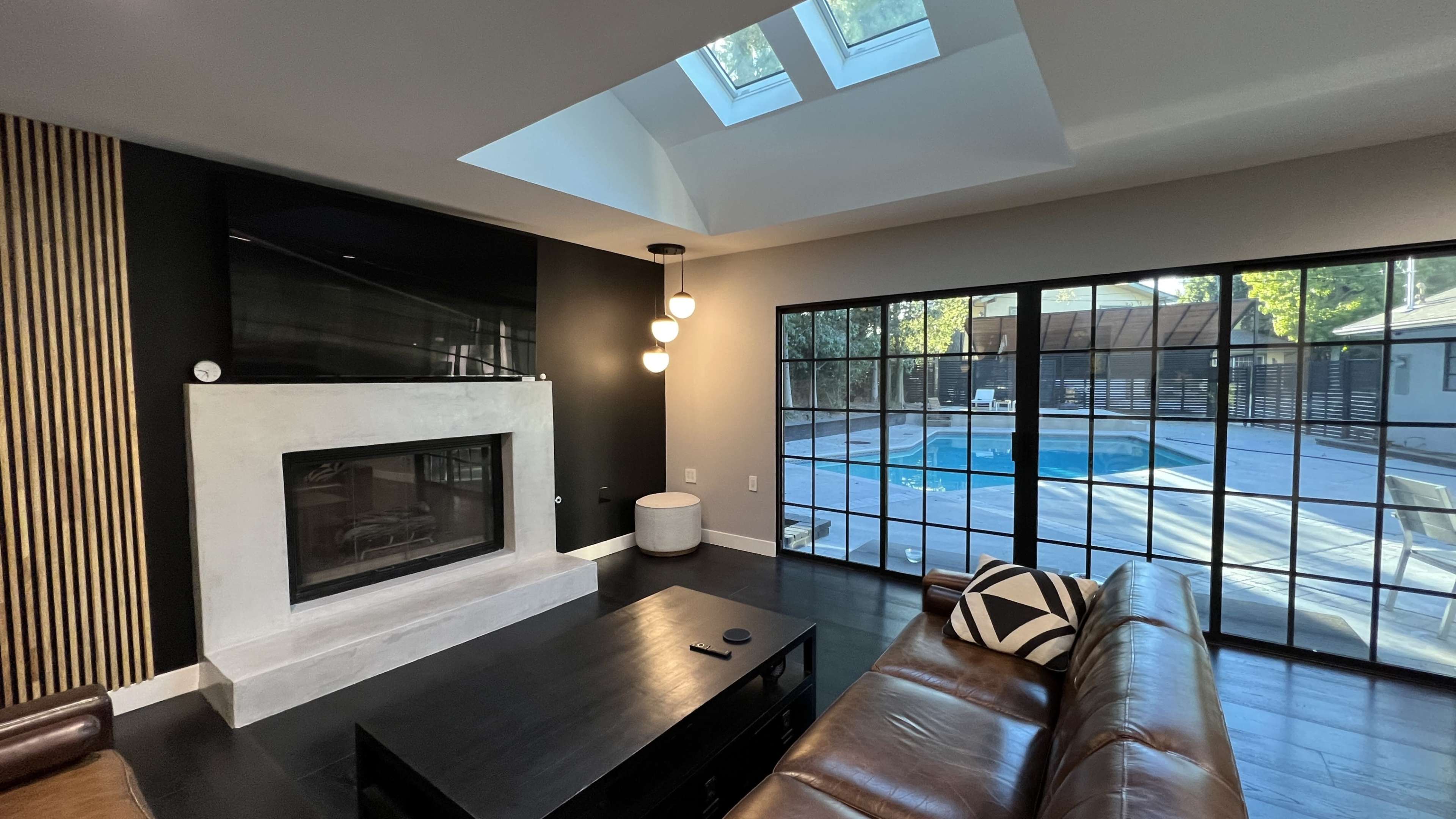 A modern living room with a fireplace, a large window overlooking a swimming pool, and a skylight above.
