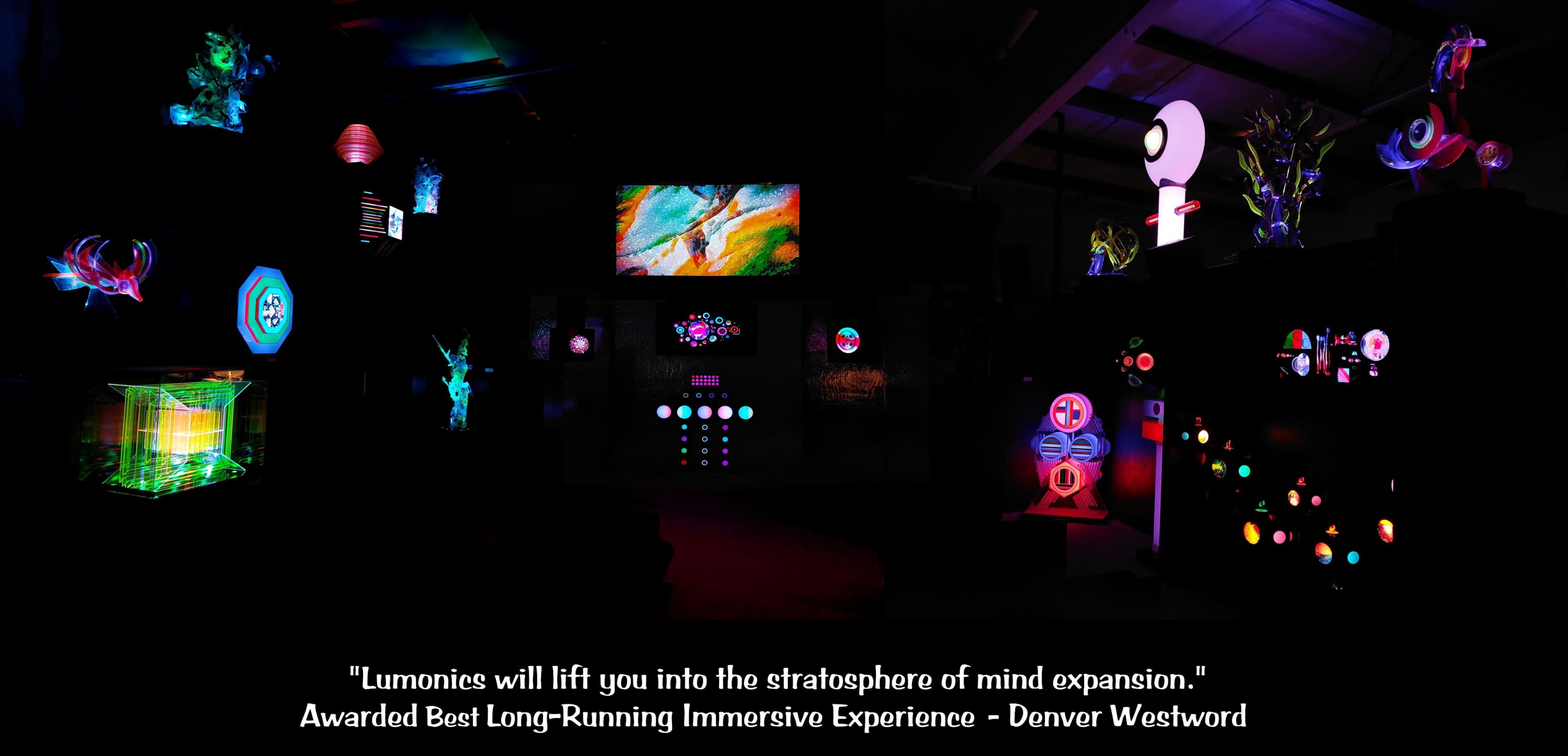 The image features a dark room filled with colorful, illuminated art installations, including geometric shapes and abstract displays.
