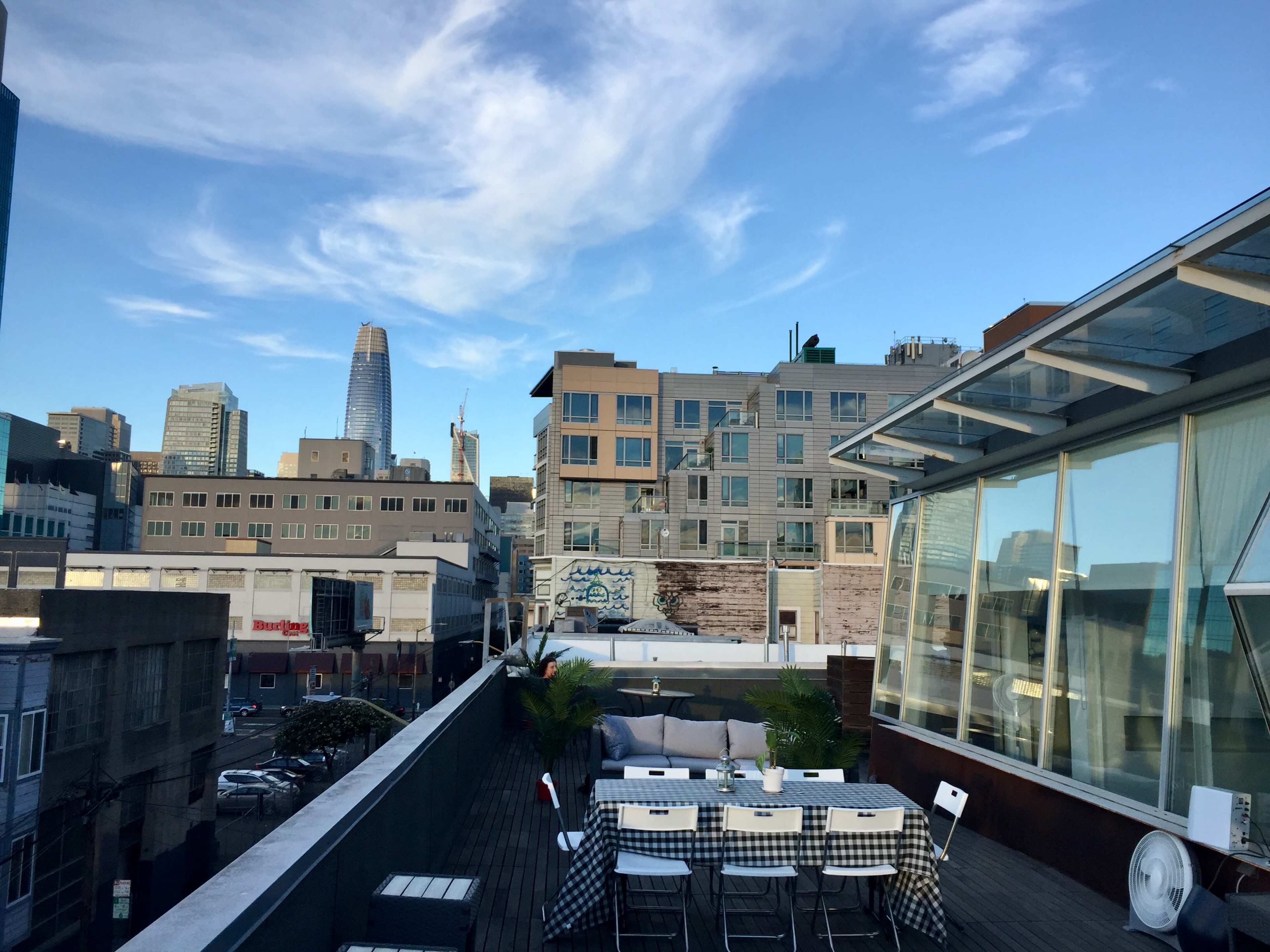 A rooftop terrace with a table and chairs overlooking a city skyline featuring modern buildings and a tall skyscraper.
