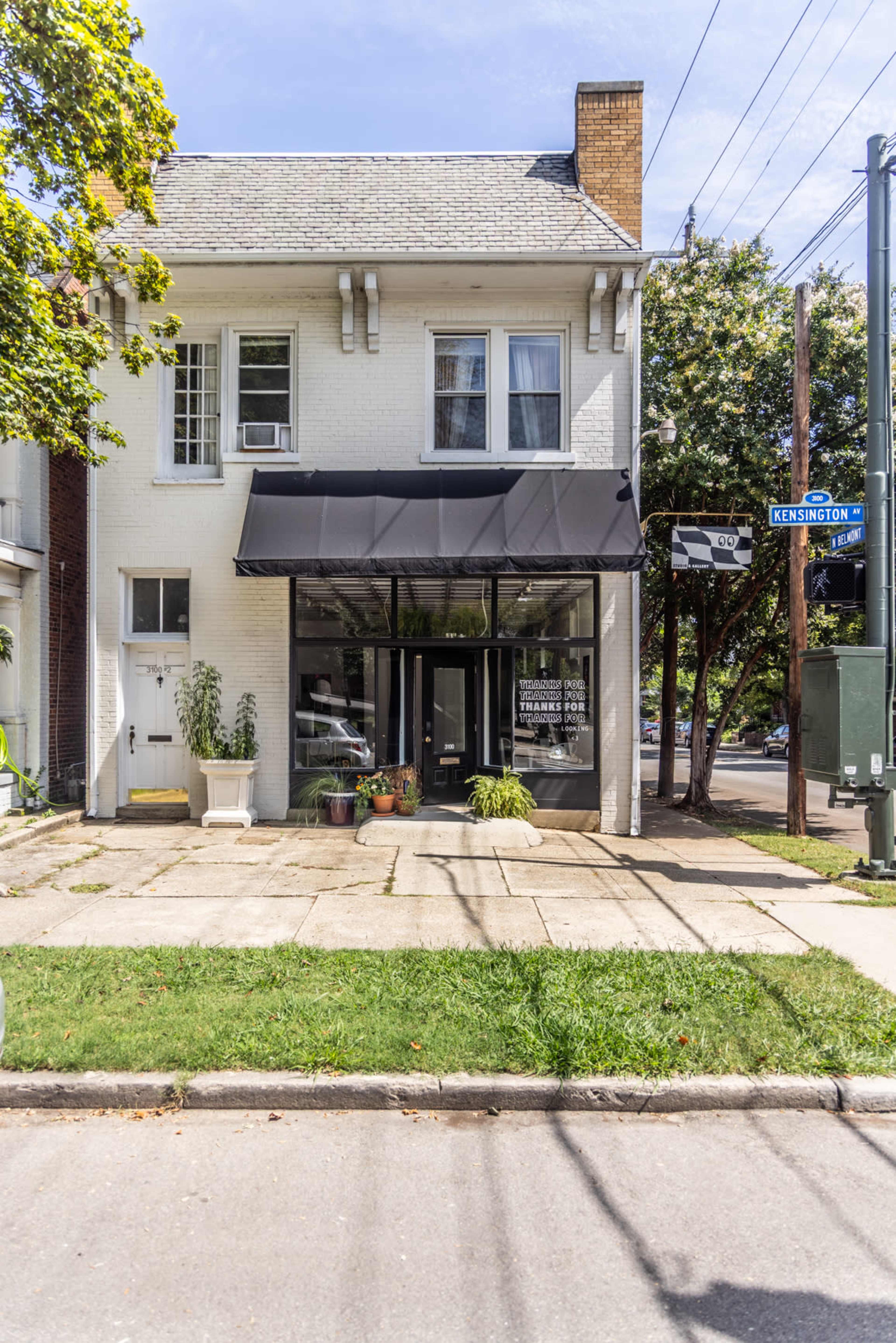 The image shows a two-story building with a black awning over the front entrance and a manicured sidewalk, located at the corner of Kensington Street.