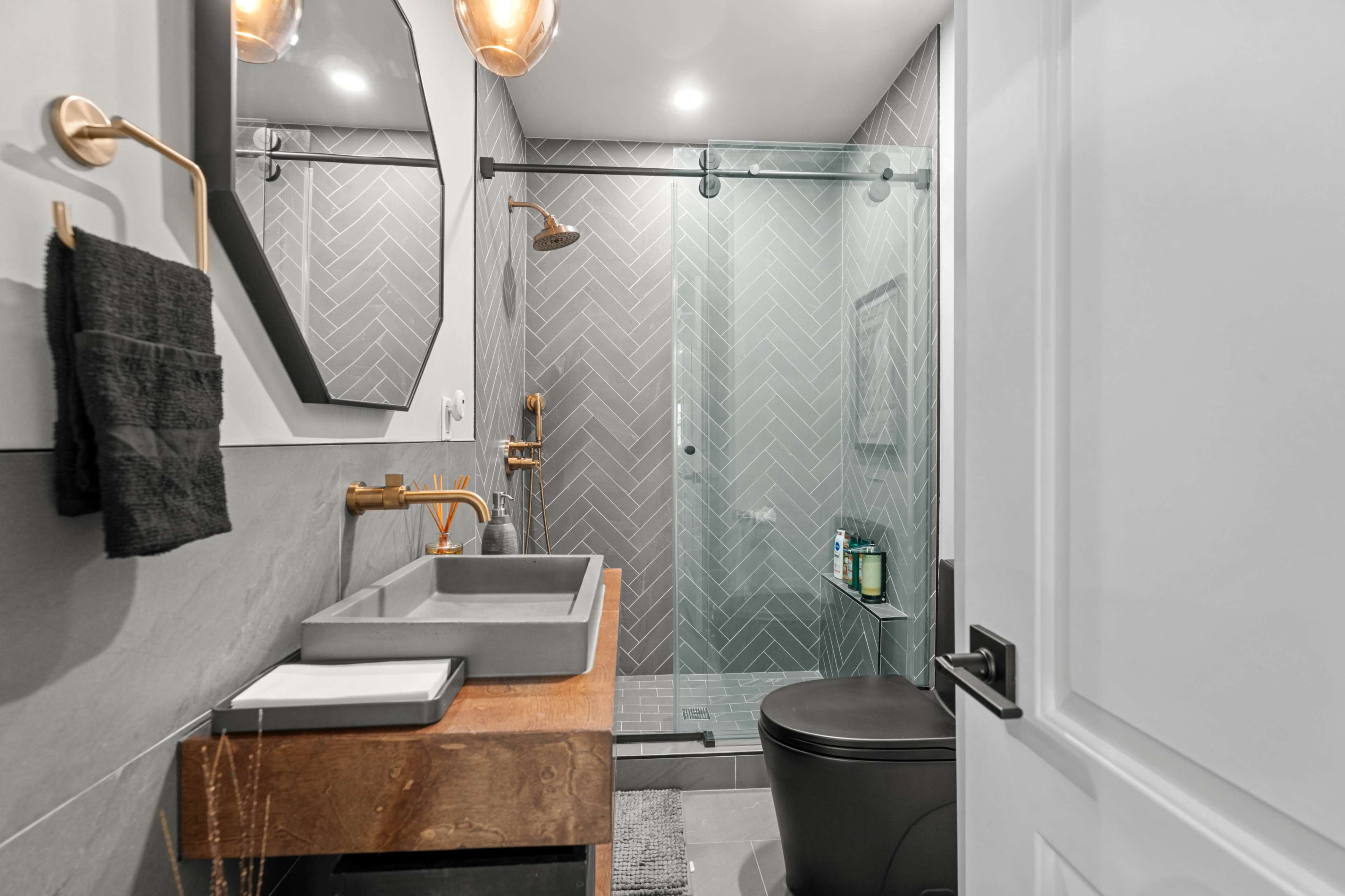 The image shows a modern bathroom with a glass shower, a wooden vanity with a sink, and neutral-colored tile walls.