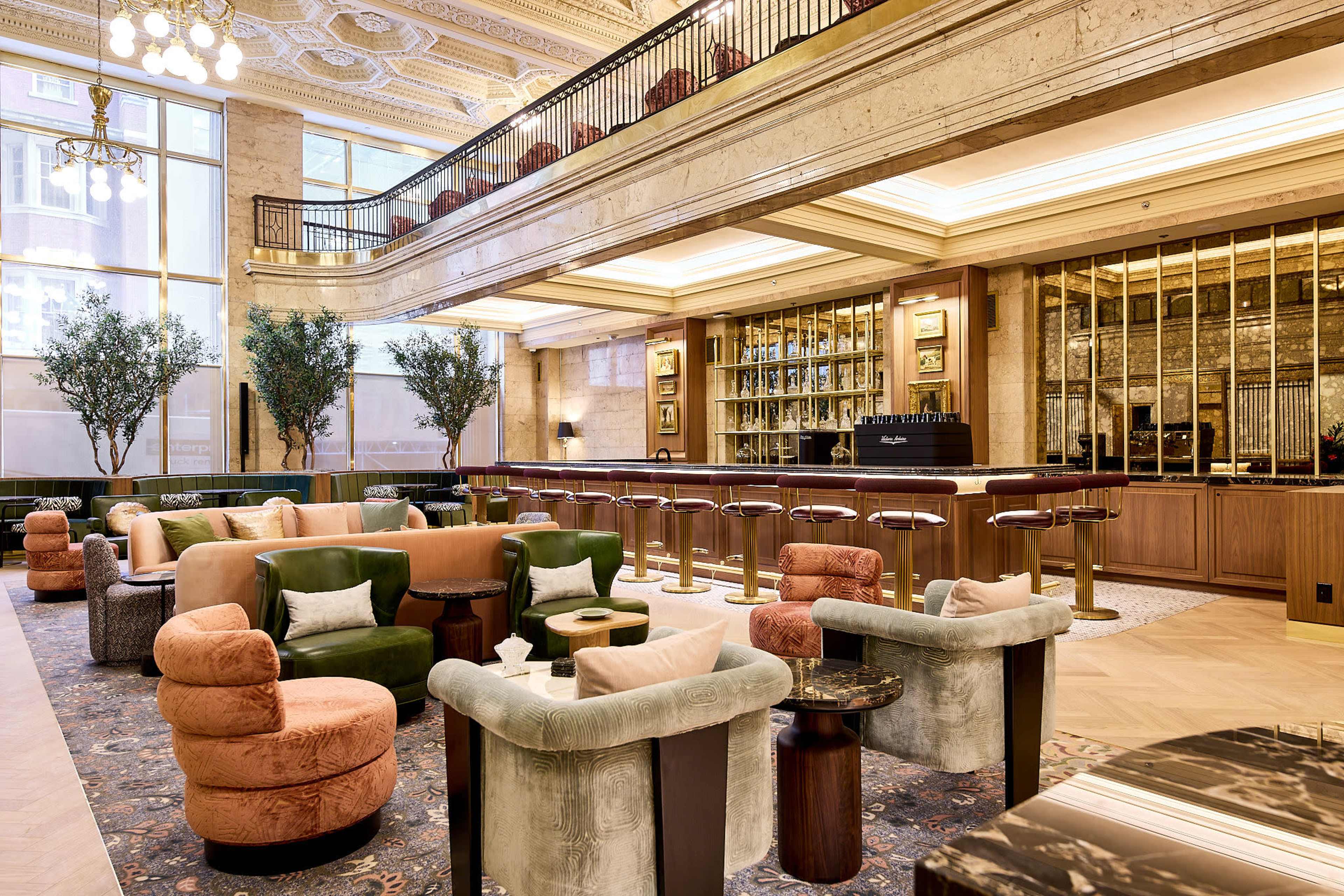 A spacious hotel lobby features a mix of plush seating, elegant decor, and a well-stocked bar in the background.