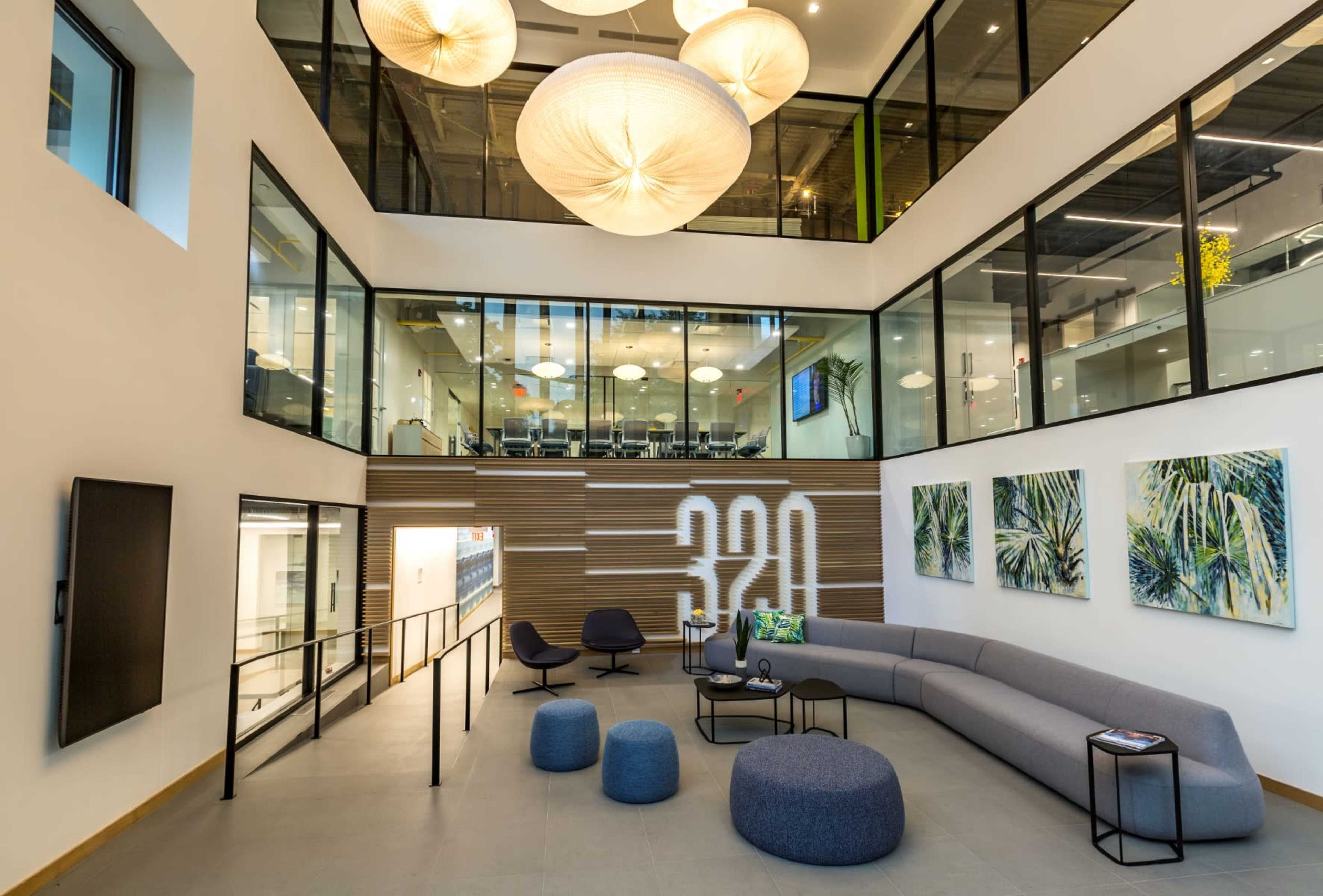 A modern multi-level lobby with large windows, a curved sofa, decorative lighting, and artwork on the walls.