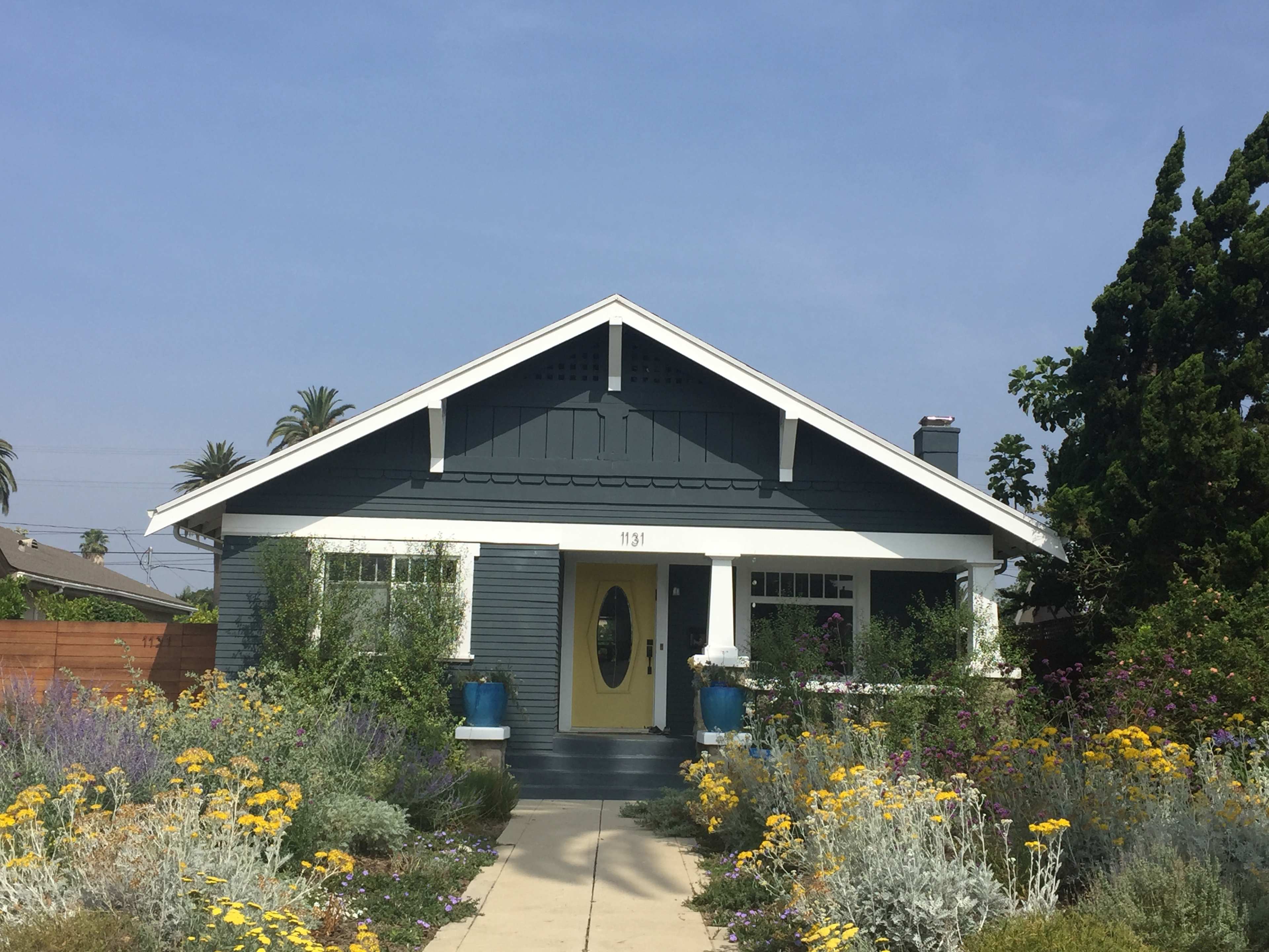 A blue house with a yellow door surrounded by a colorful flower garden and palm trees in the background.