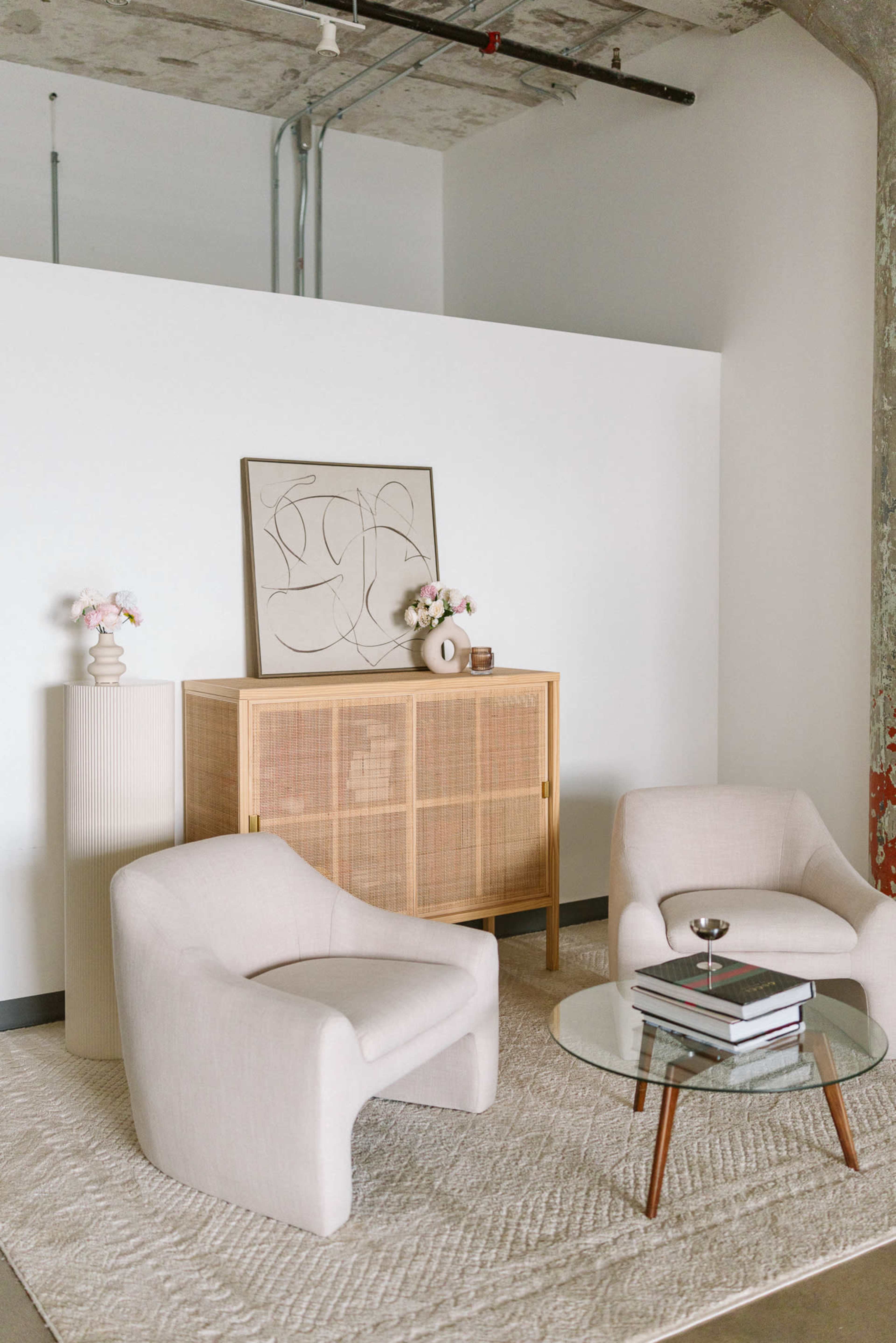 The image features a cozy interior setting with two curved chairs, a glass coffee table, and a wooden cabinet adorned with decorative items and artwork.
