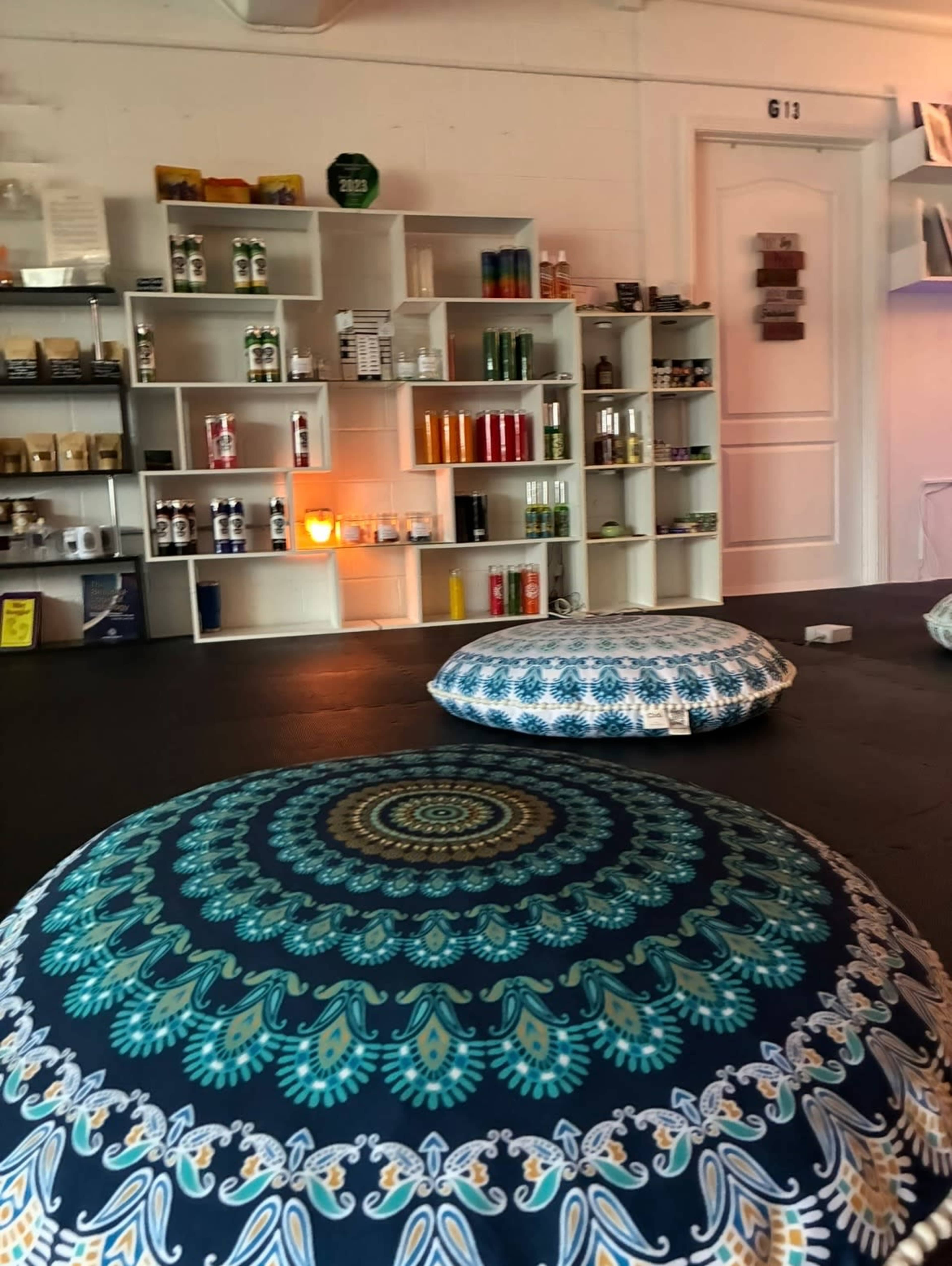 A room features colorful floor cushions and shelves stocked with various beverages and products.